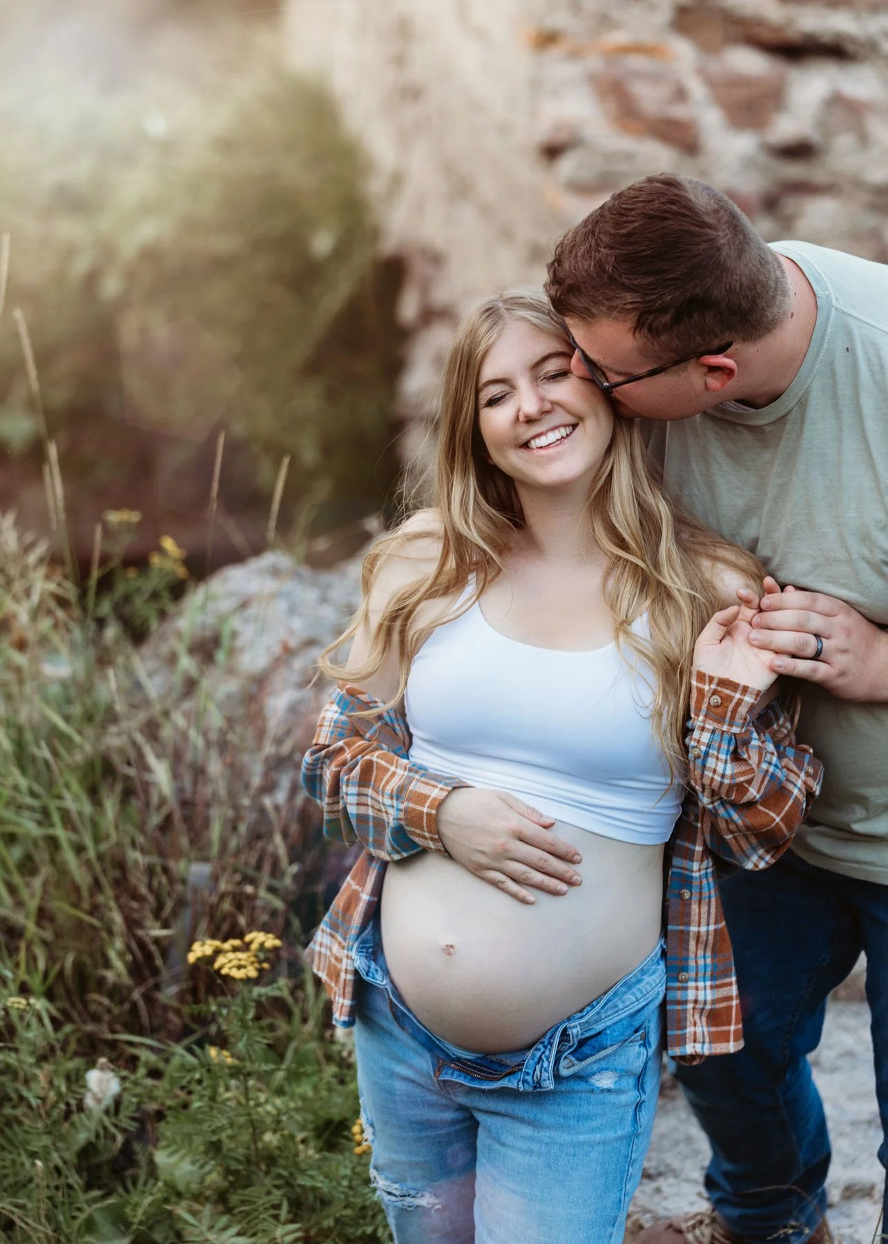 Couple posing in front of river holding baby bump and kissing