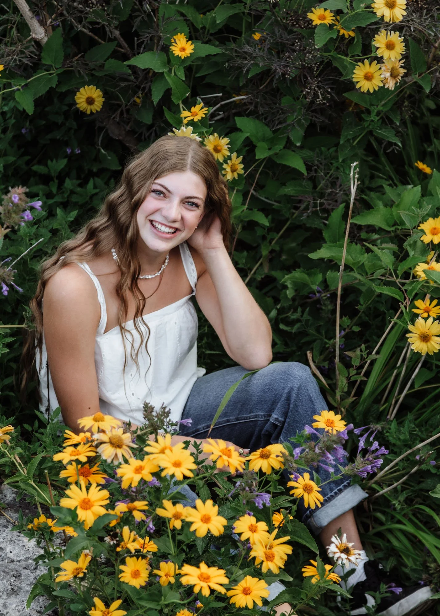 Senior girl sitting in field of yellow flowers smiling