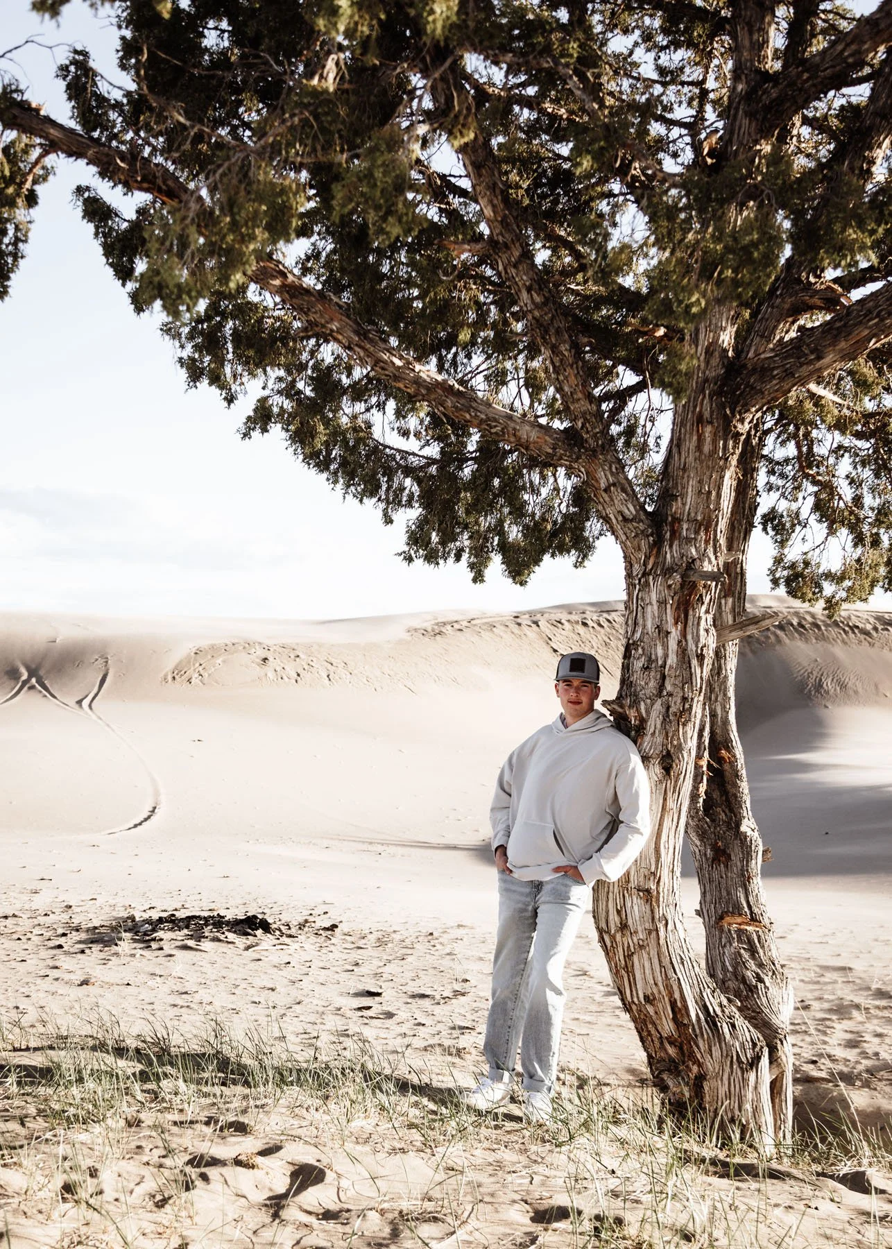 Senior boy standing by tree with sand dunes in background