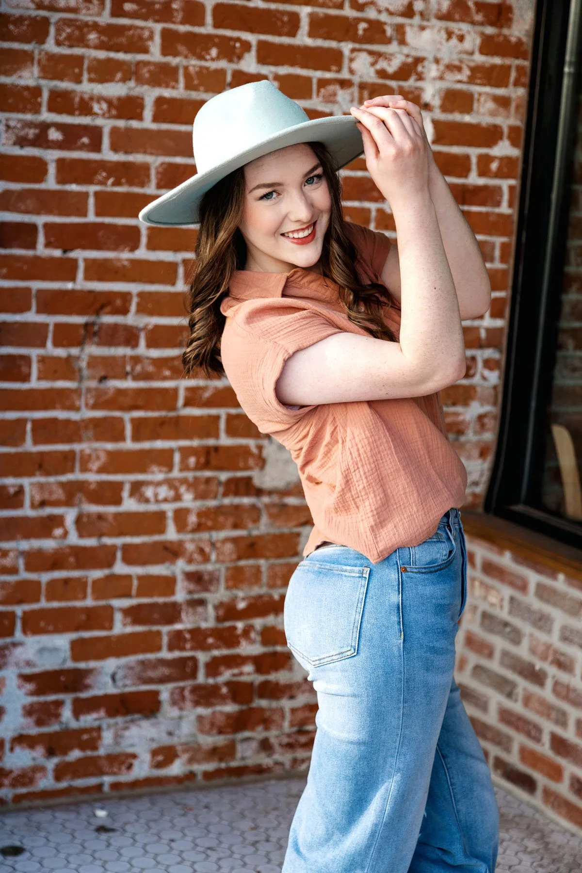 Senior girl peeking from behind brick wall in orange shirt