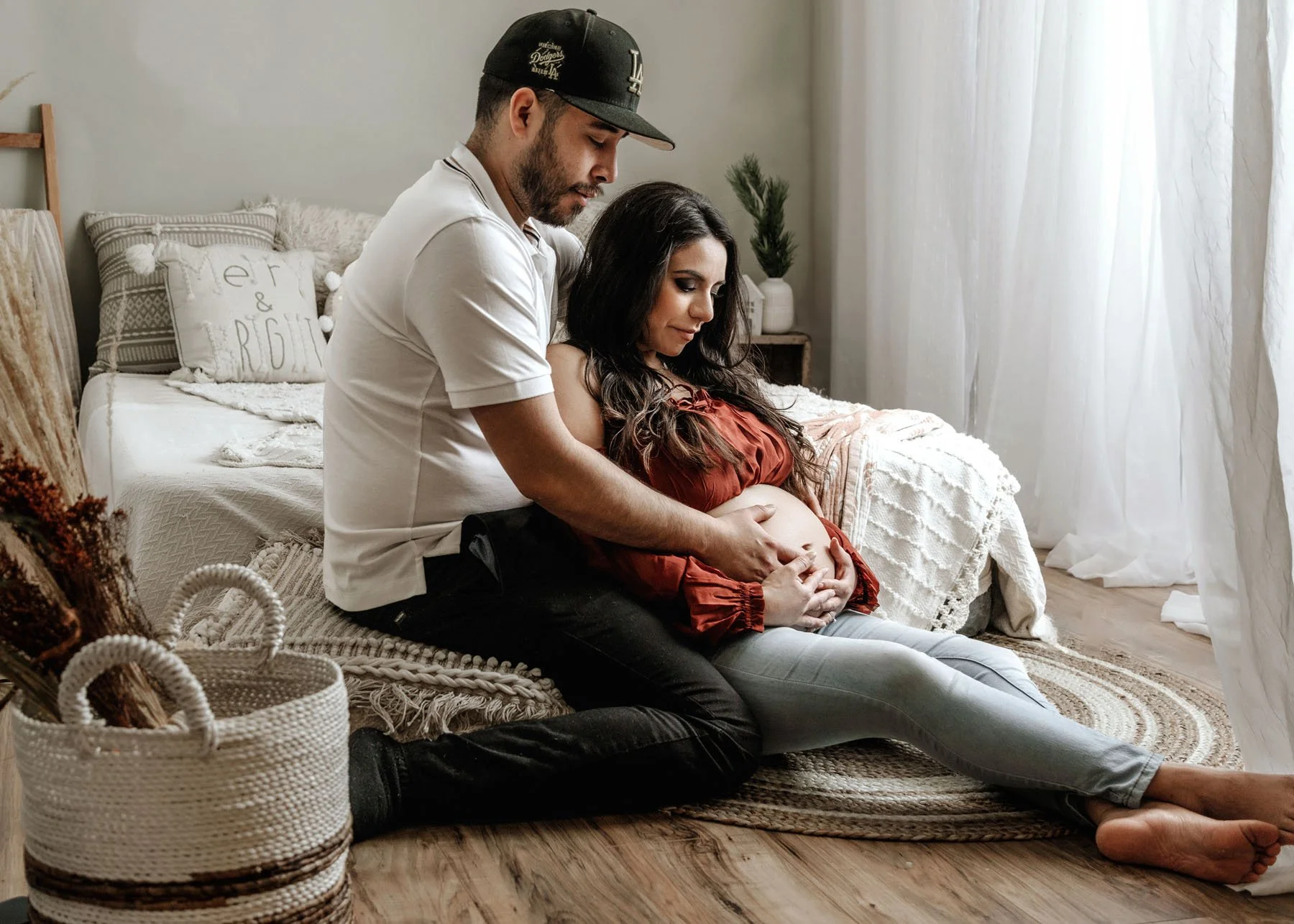 Expecting couple sitting in front of bed, daddy's hand on mama's baby bump