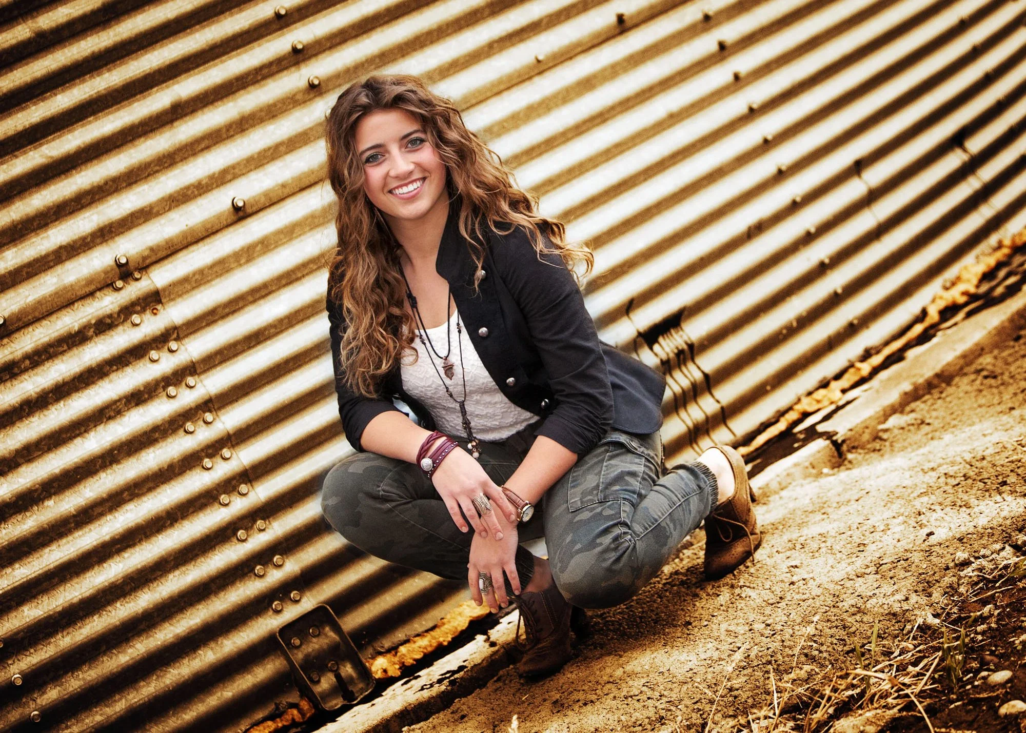 Senior girl squatting in front of green silo for outdoor portrait