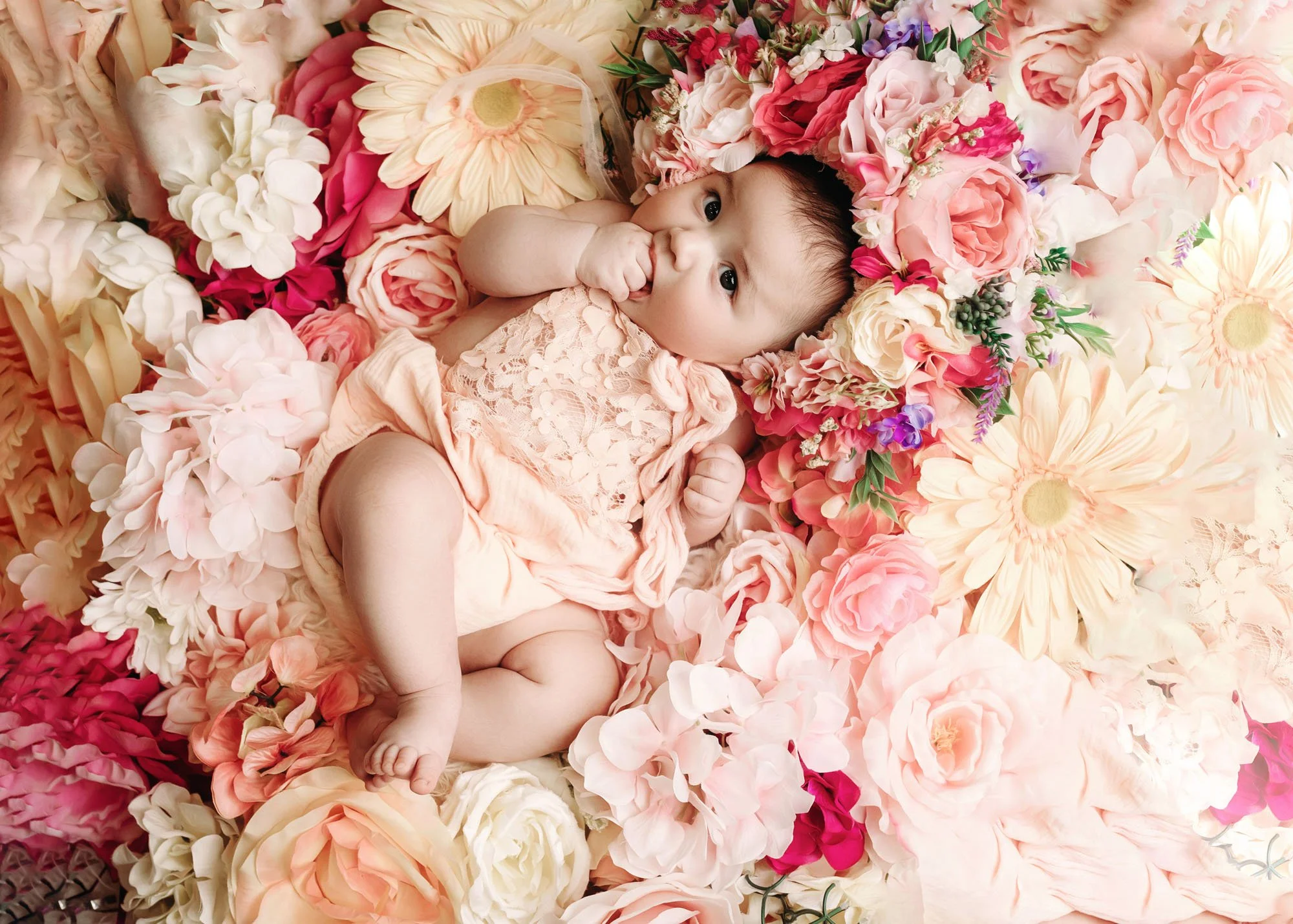 Infant lying in bed of flowers with floral hat for milestone session