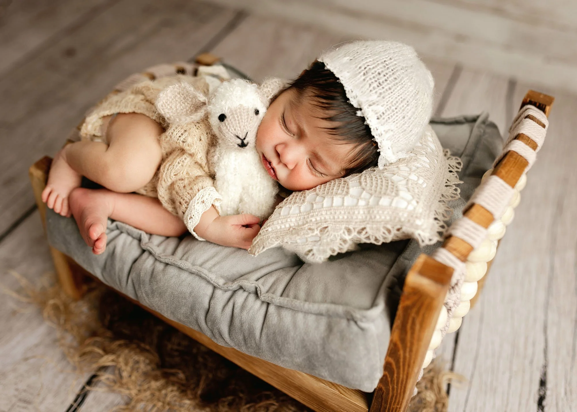 Newborn in miniature bed holding stuffed lamb prop