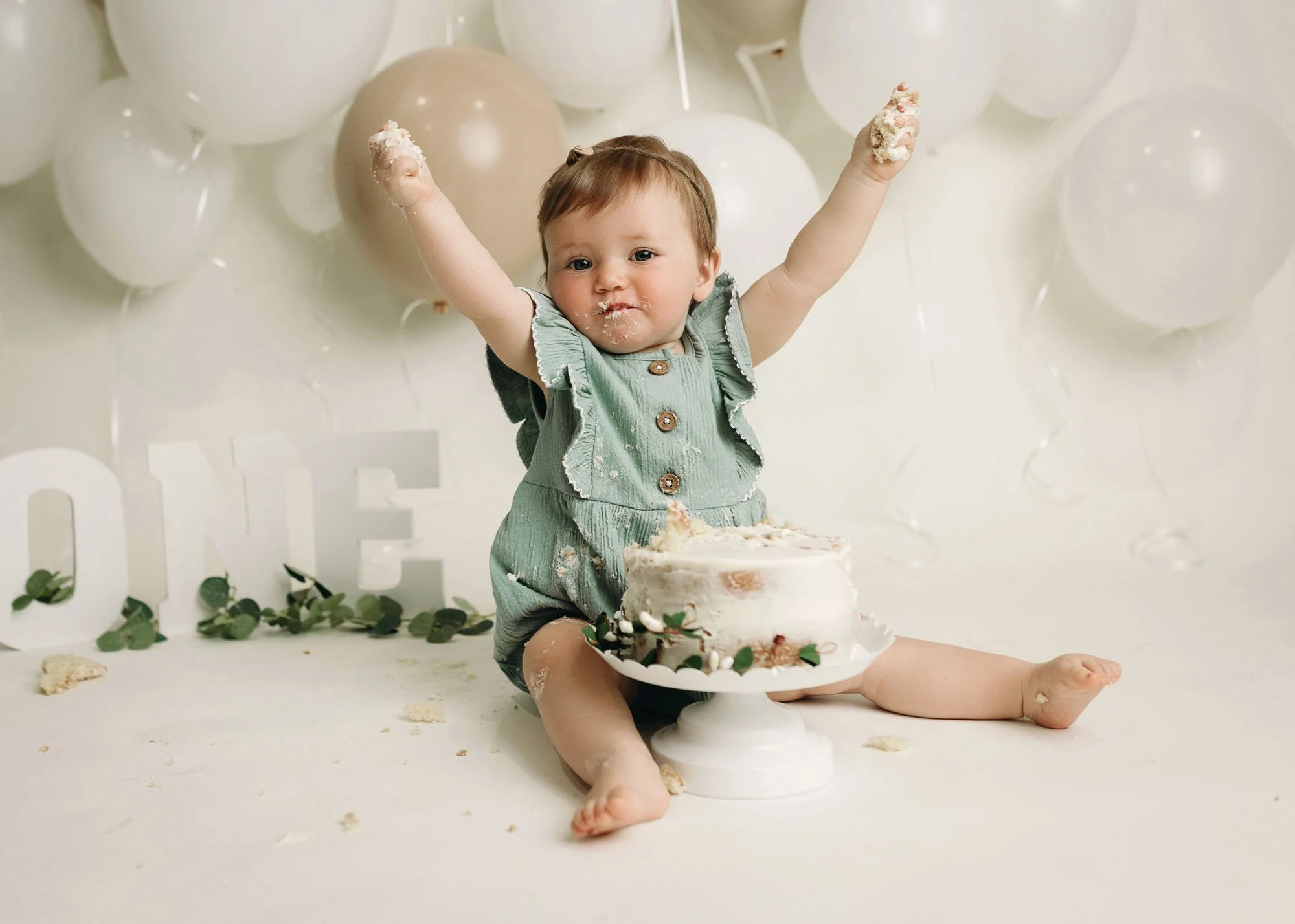 One year old girl with white cake and green balloons