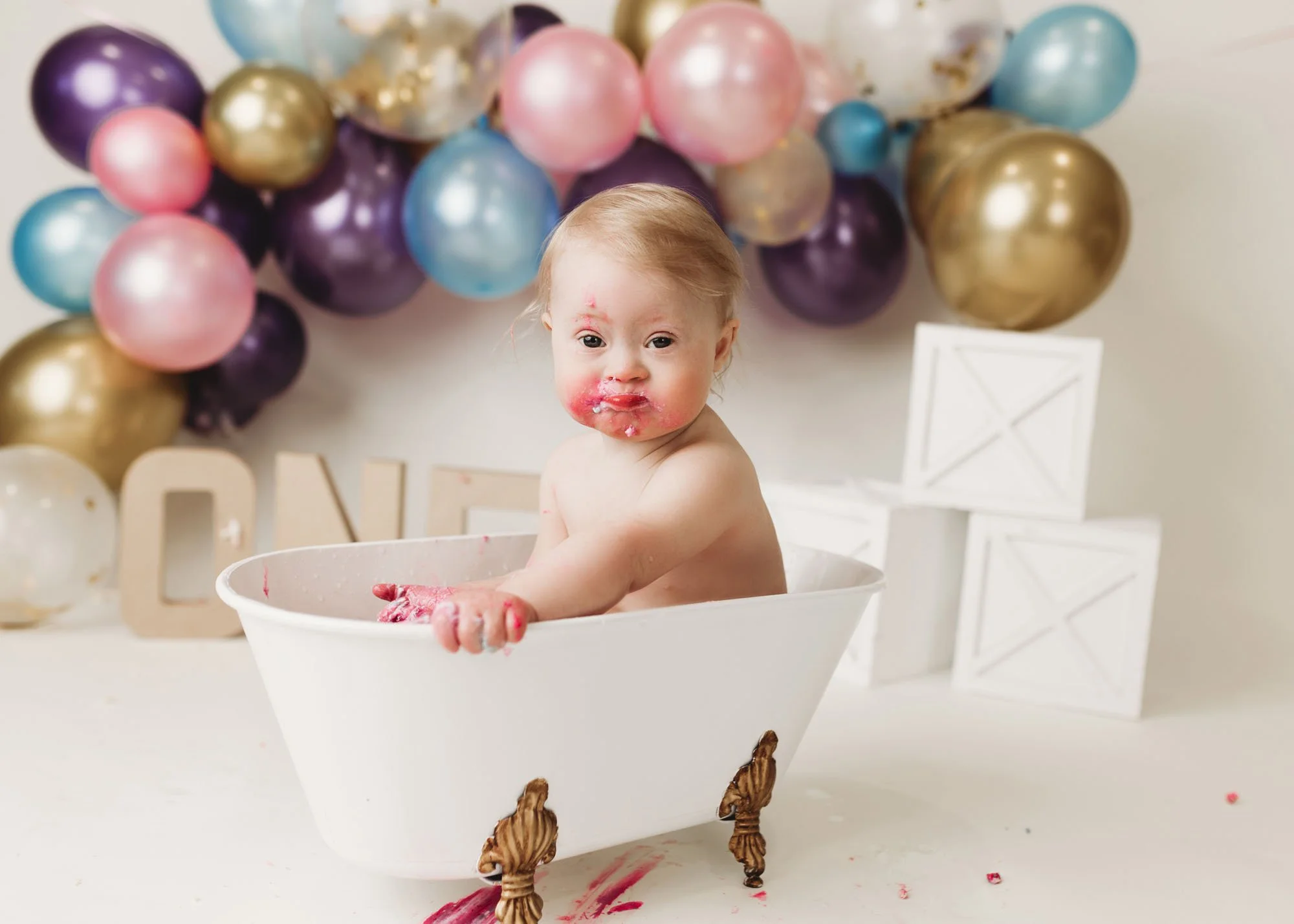 Baby girl enjoying colorful themed cake smash in small studio tub