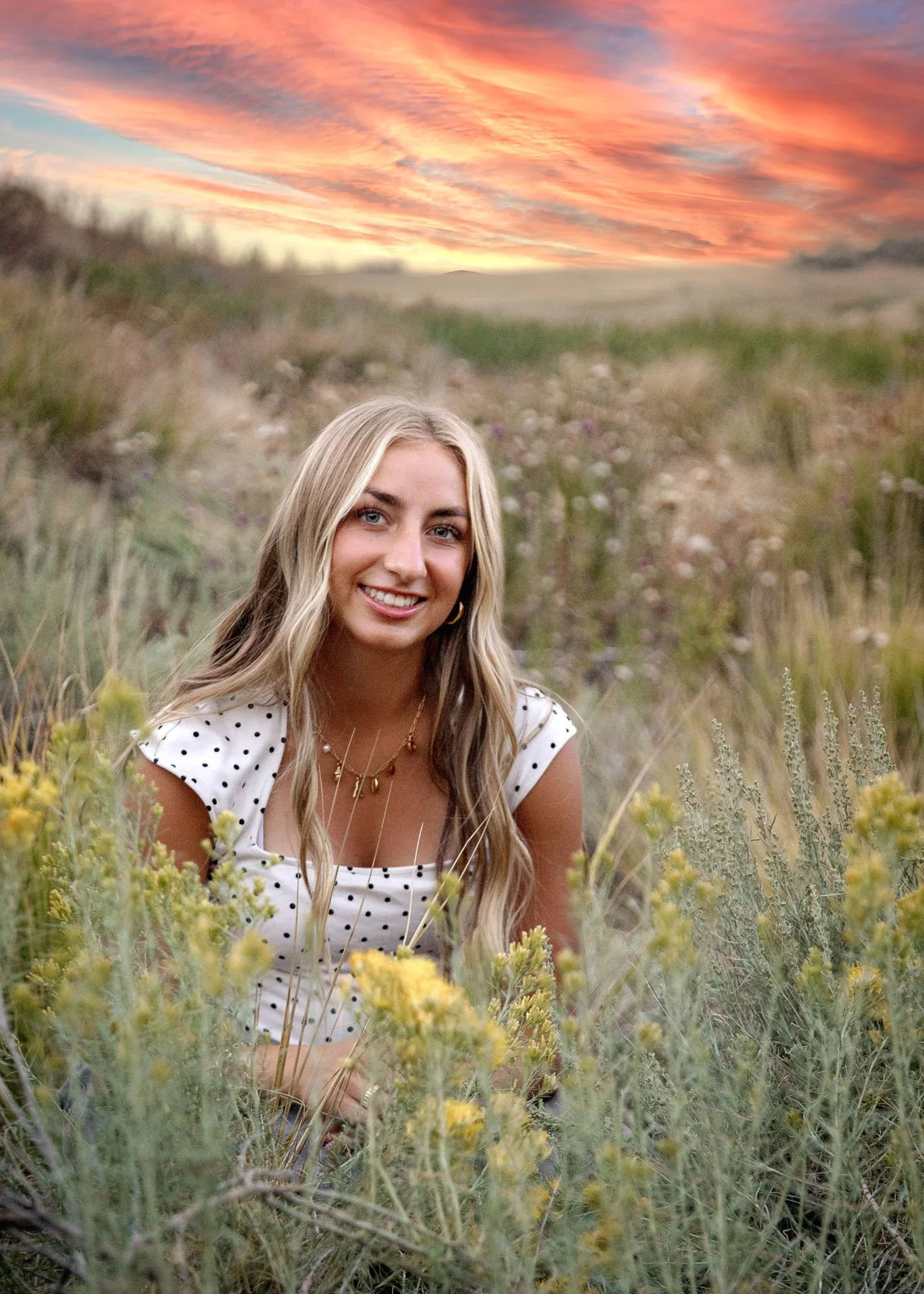 Senior girl sitting in field of flowers with sunset behind her