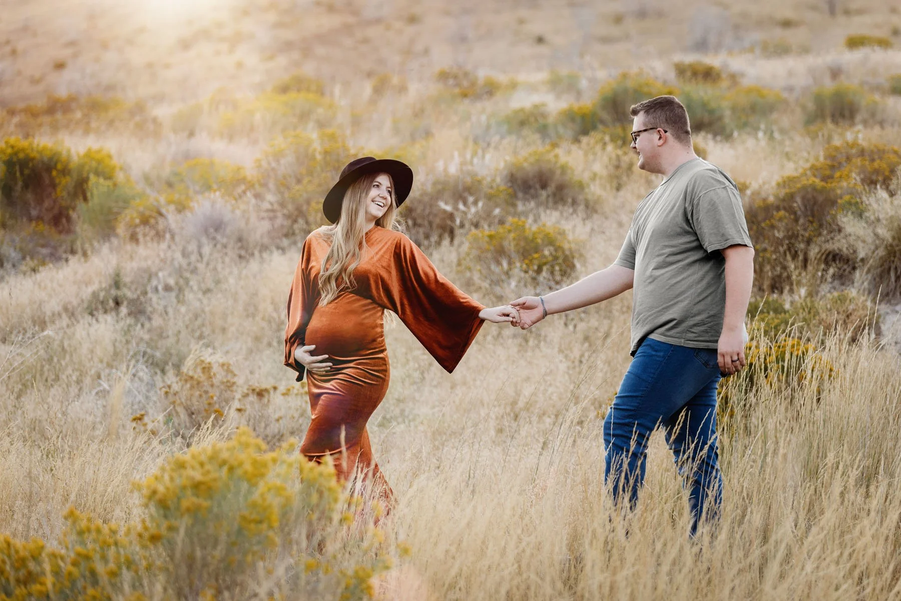 Mama in orange dress walking in tall grass and yellow sagebrush, daddy walking behind holding her hand