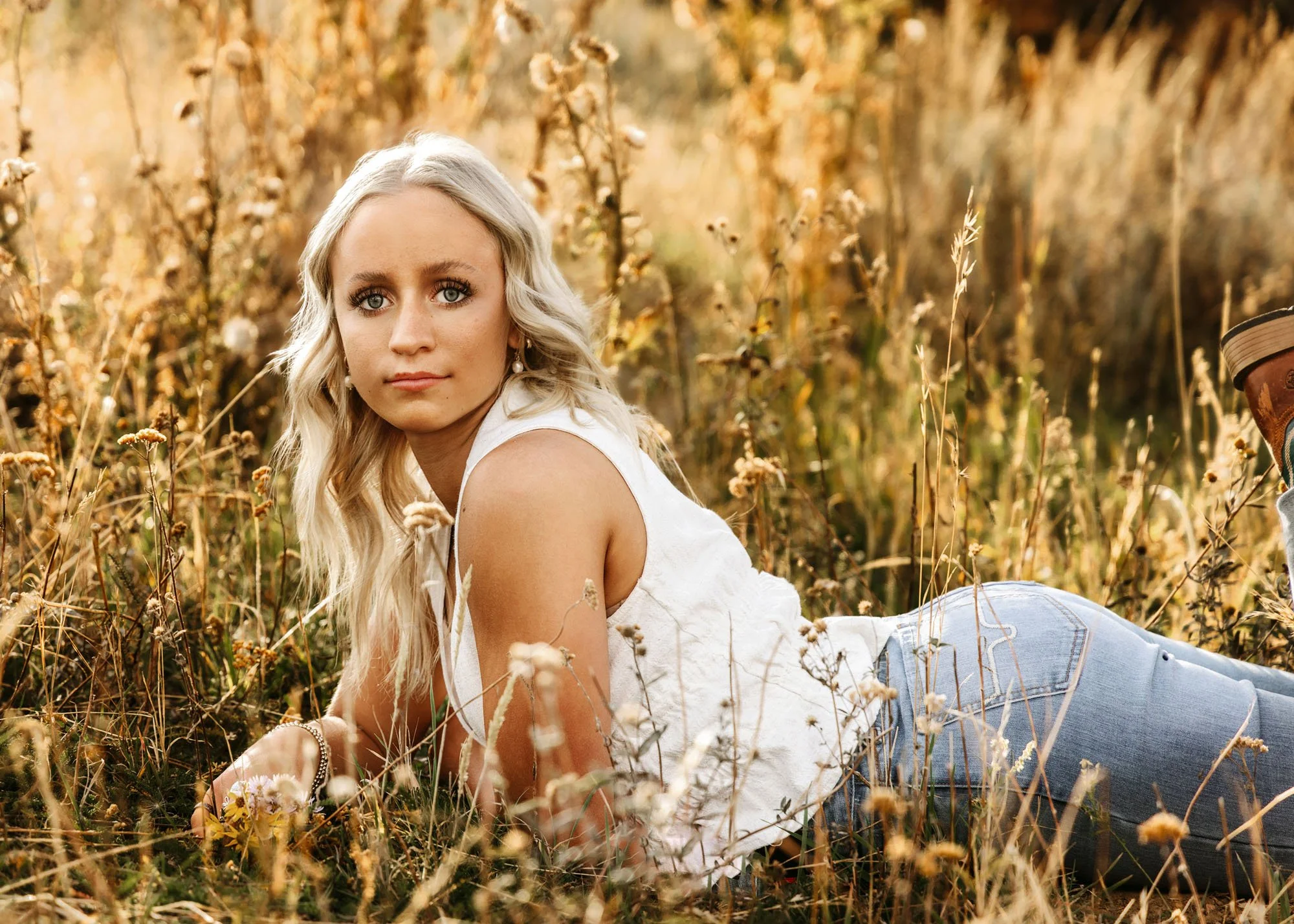 Senior girl laying on tummy in tall weeds for outdoor portrait