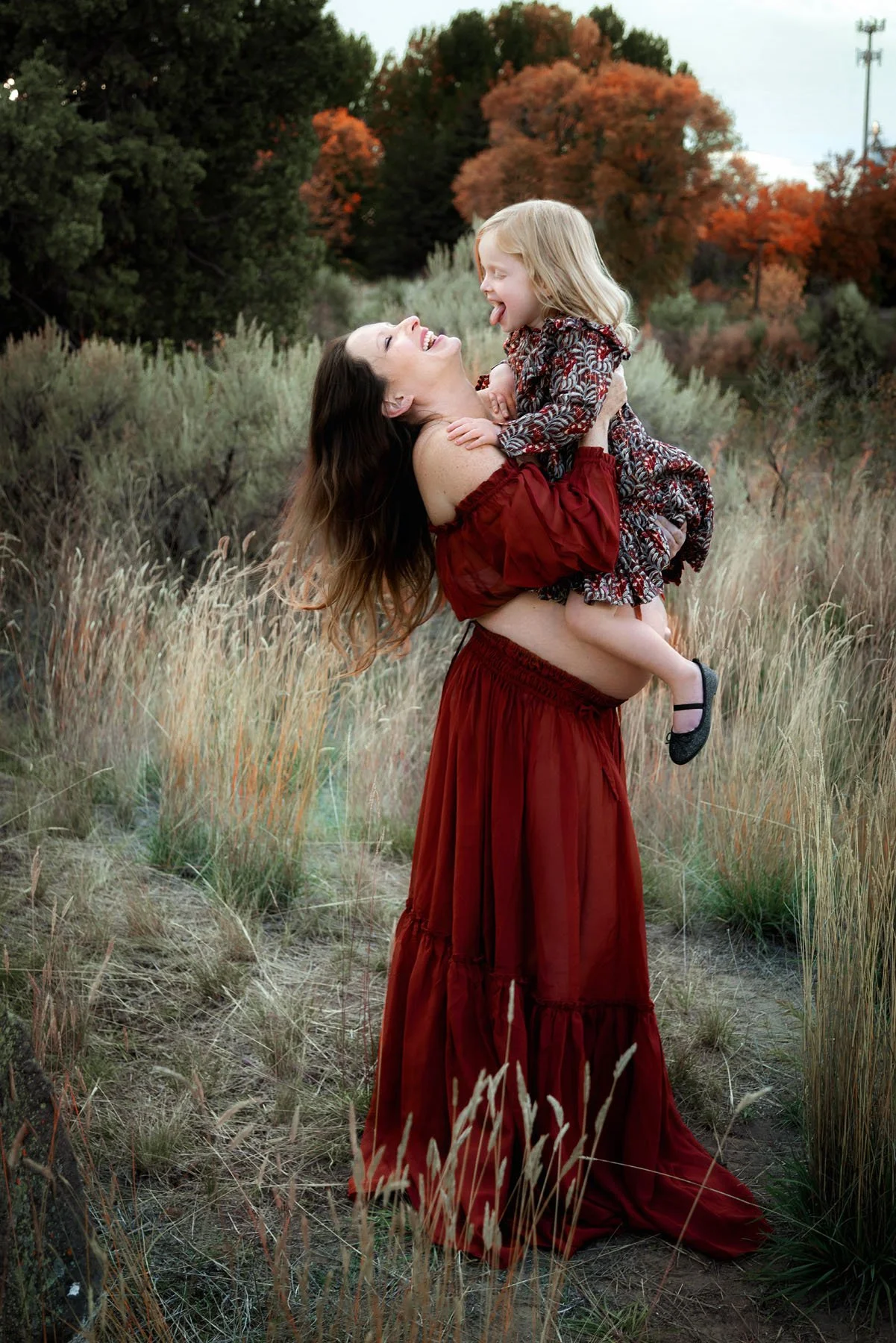 Mama in red top and skirt holding baby bump and lifting toddler outdoors