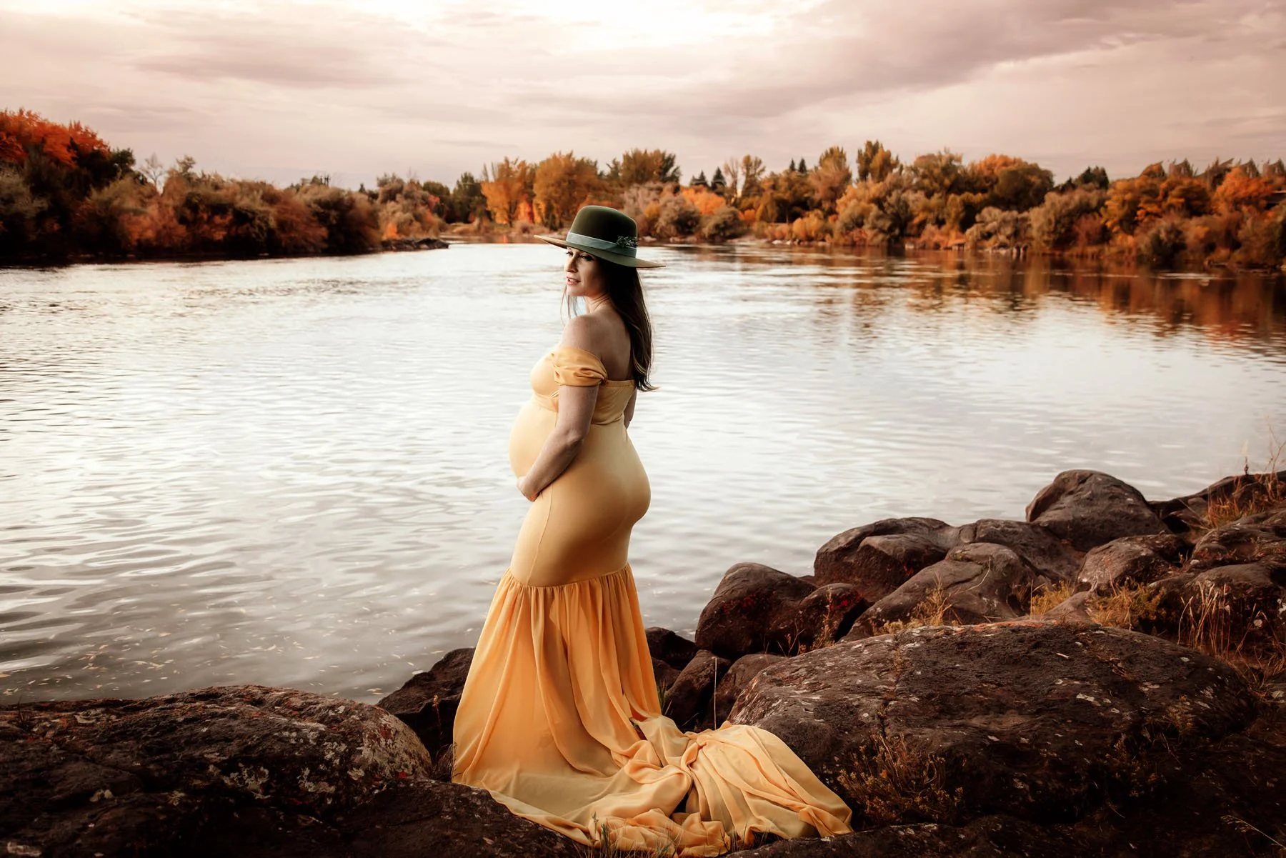 mama in yellow dress by river holding baby bump looking away