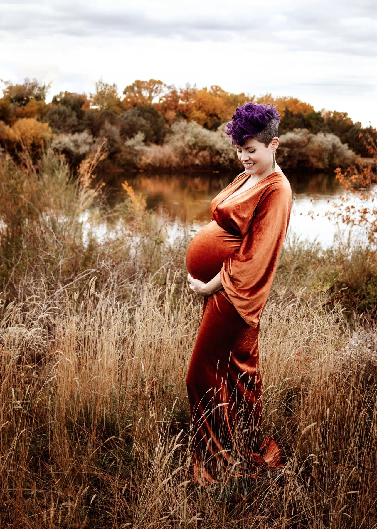 mama in orange velvet  dress in tall grass holding baby bump