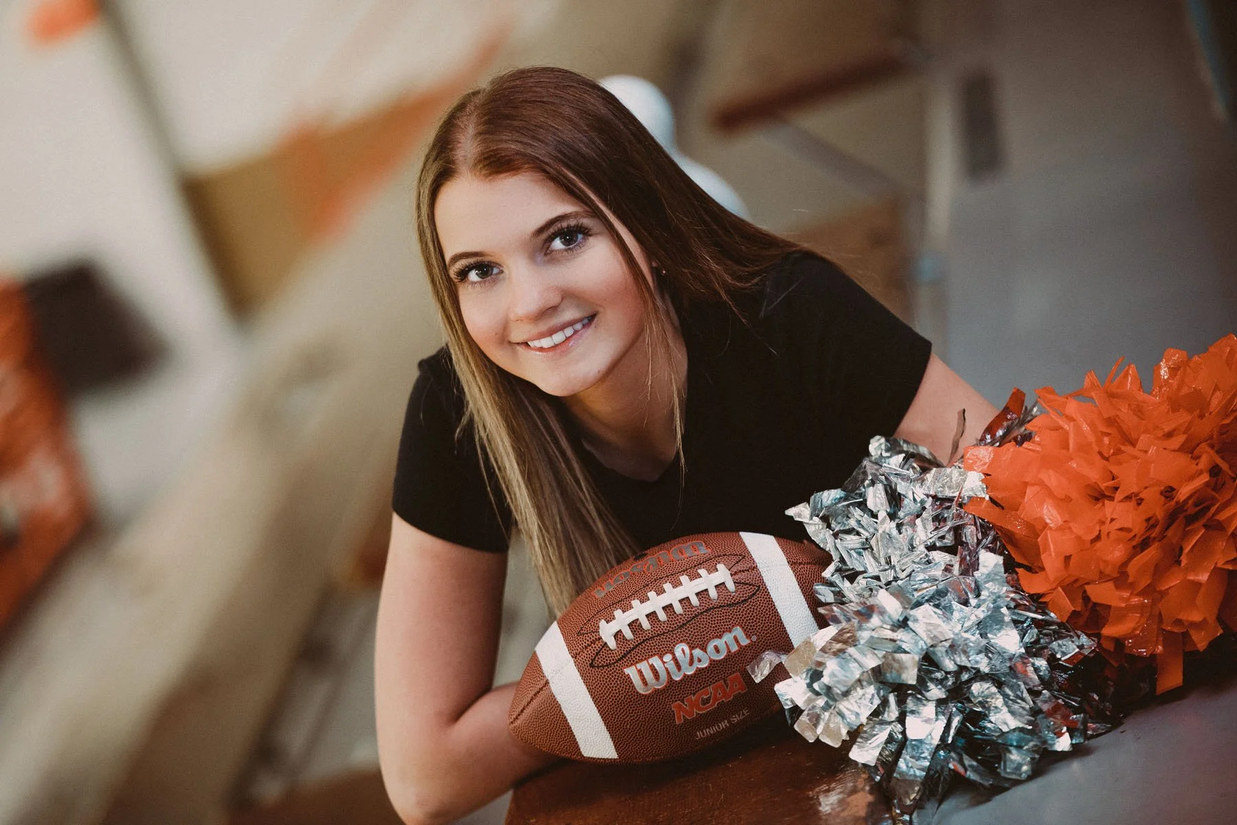 Senior girl laying on tummy on gym bleachers with football and cheer palms