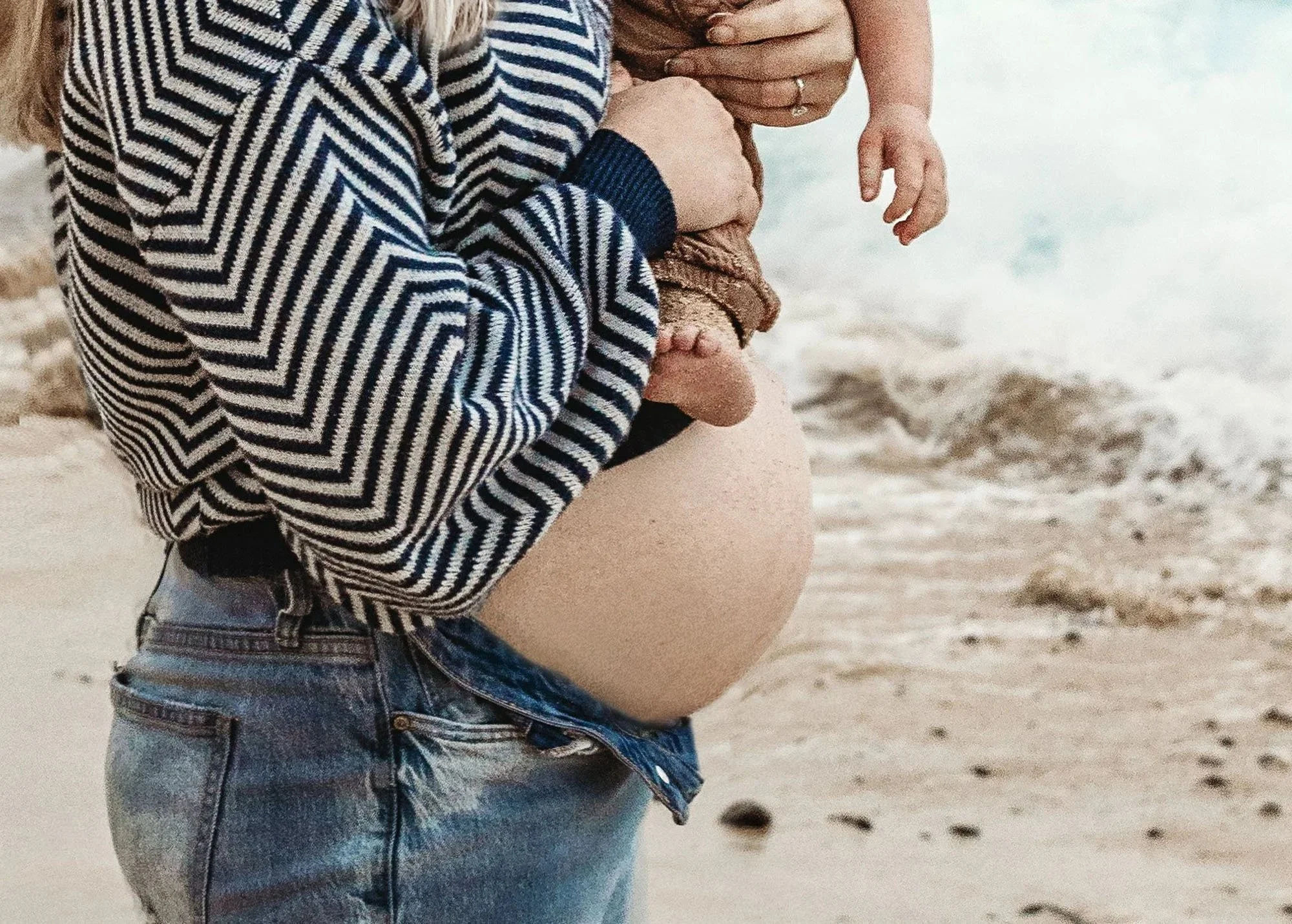 Couple kissing on the beach, mama holding baby bump while toddler sits on daddy's shoulders