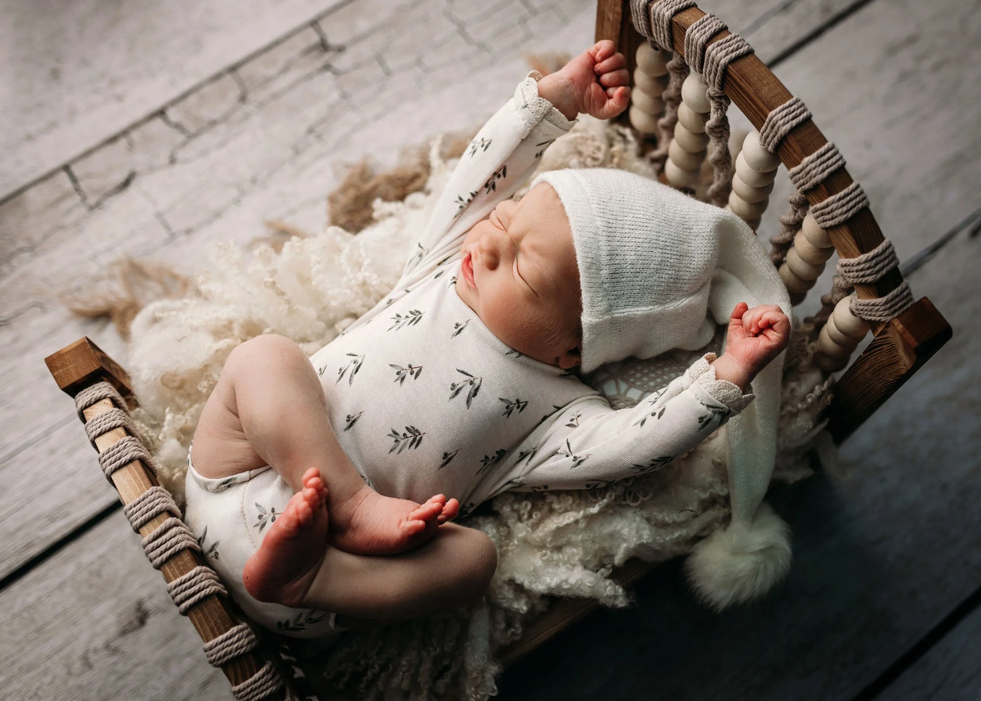 Newborn posed on tummy with legs hanging over miniature bed
