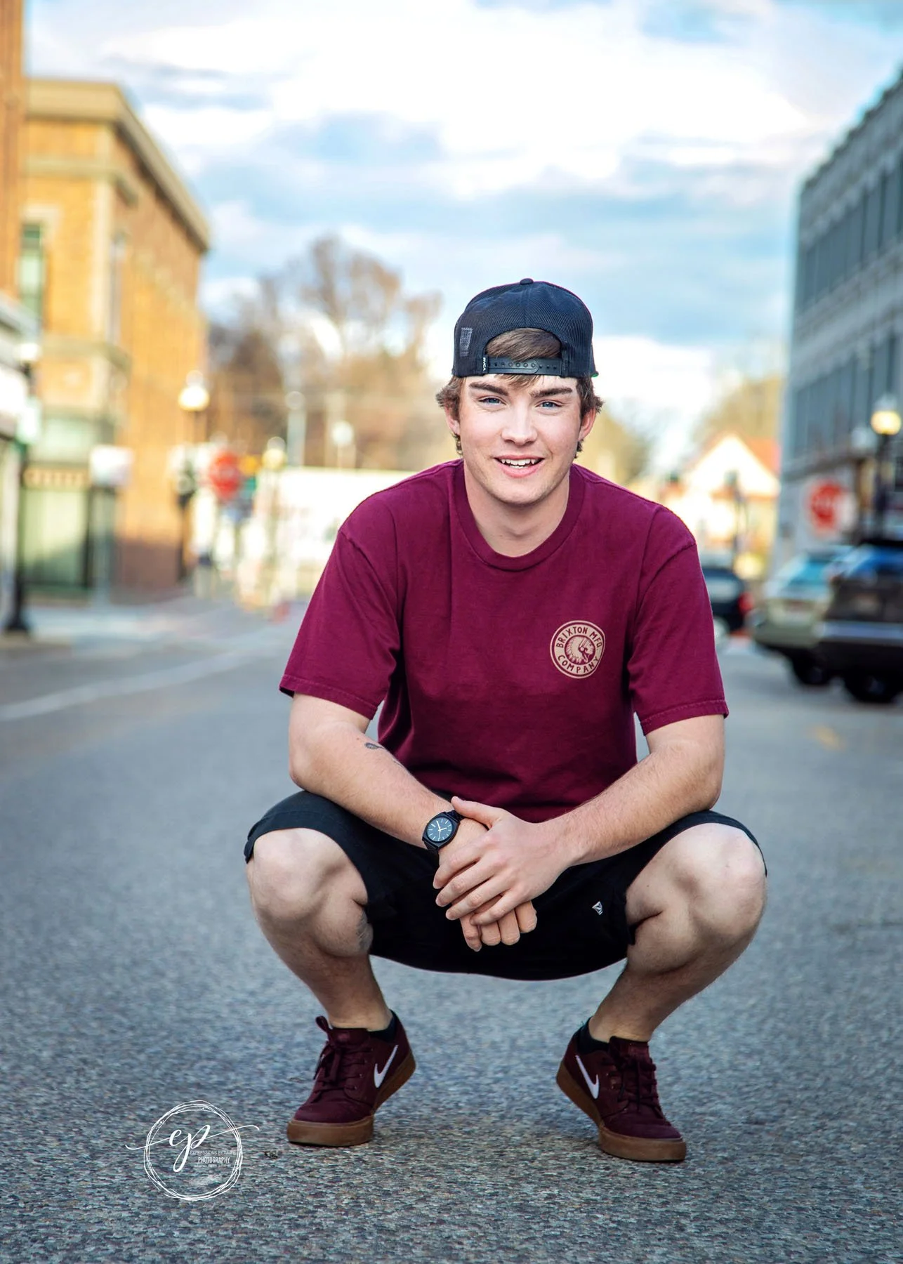 Senior boy squatting in middle of downtown street for senior portrait