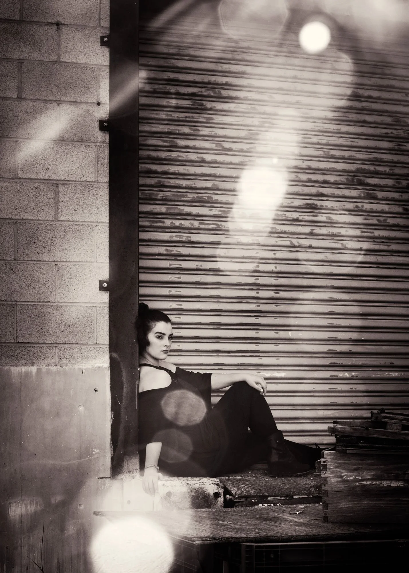 Teen girl sitting with back against wall near green silo outdoors
