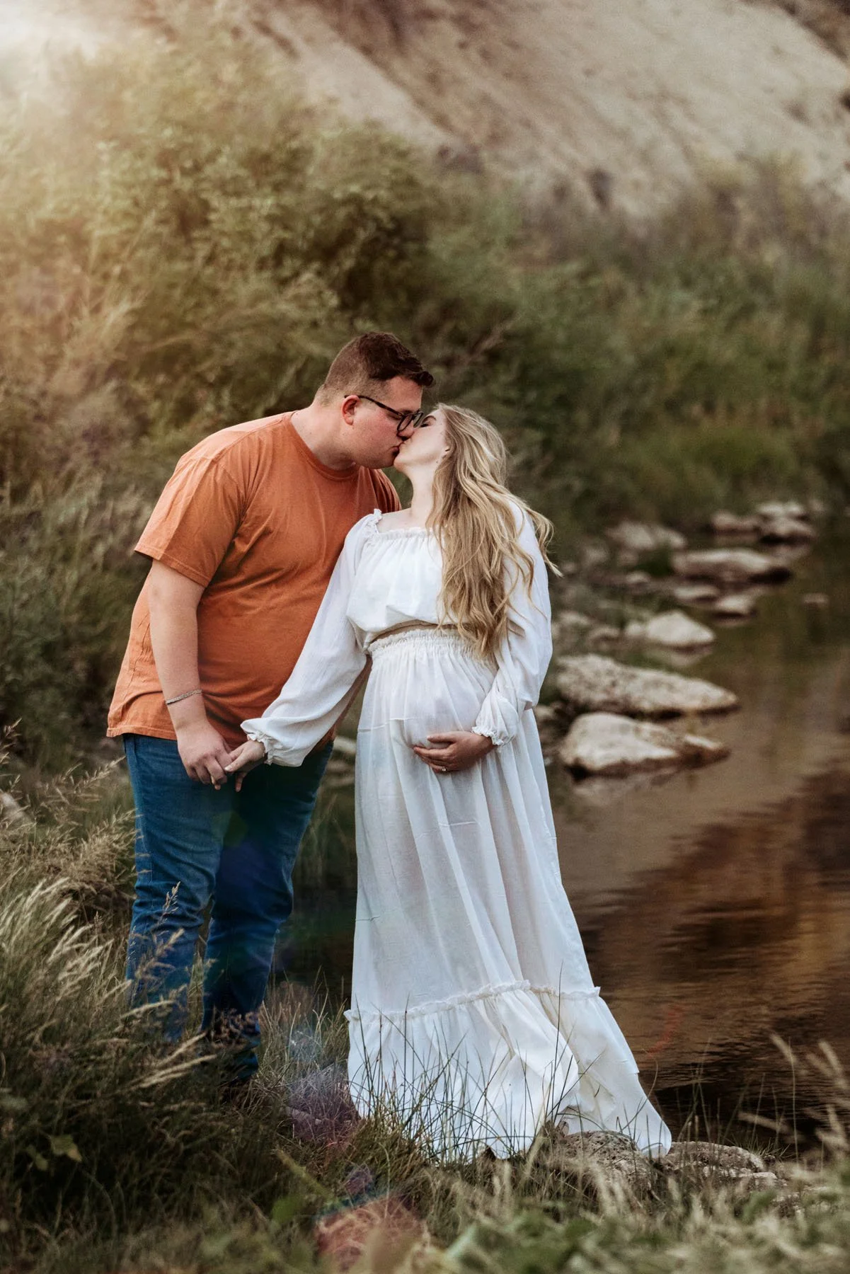 Couple in mountains with pine trees and sunset behind, baby bump visible