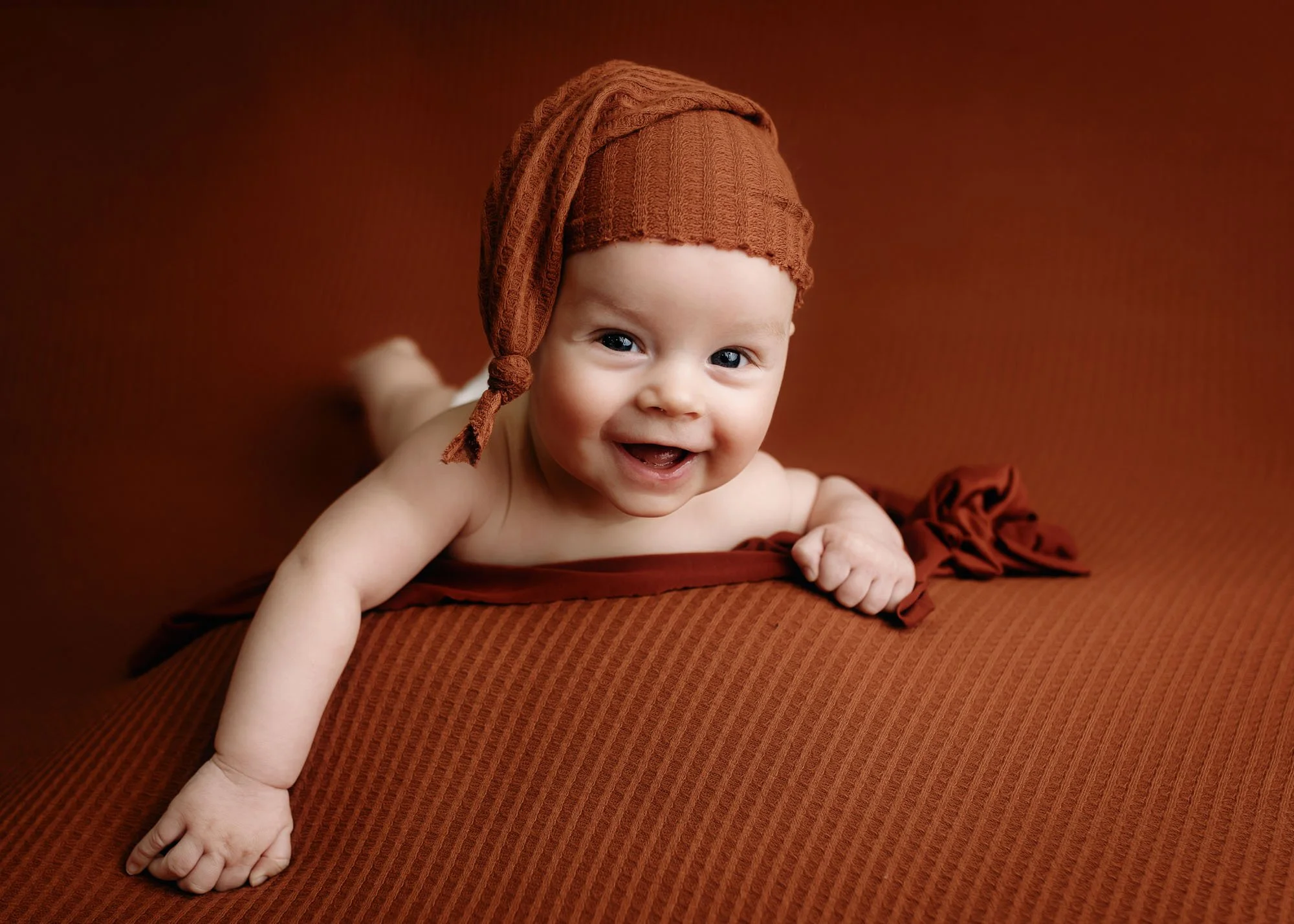 Baby lying on tummy with big smile during milestone session