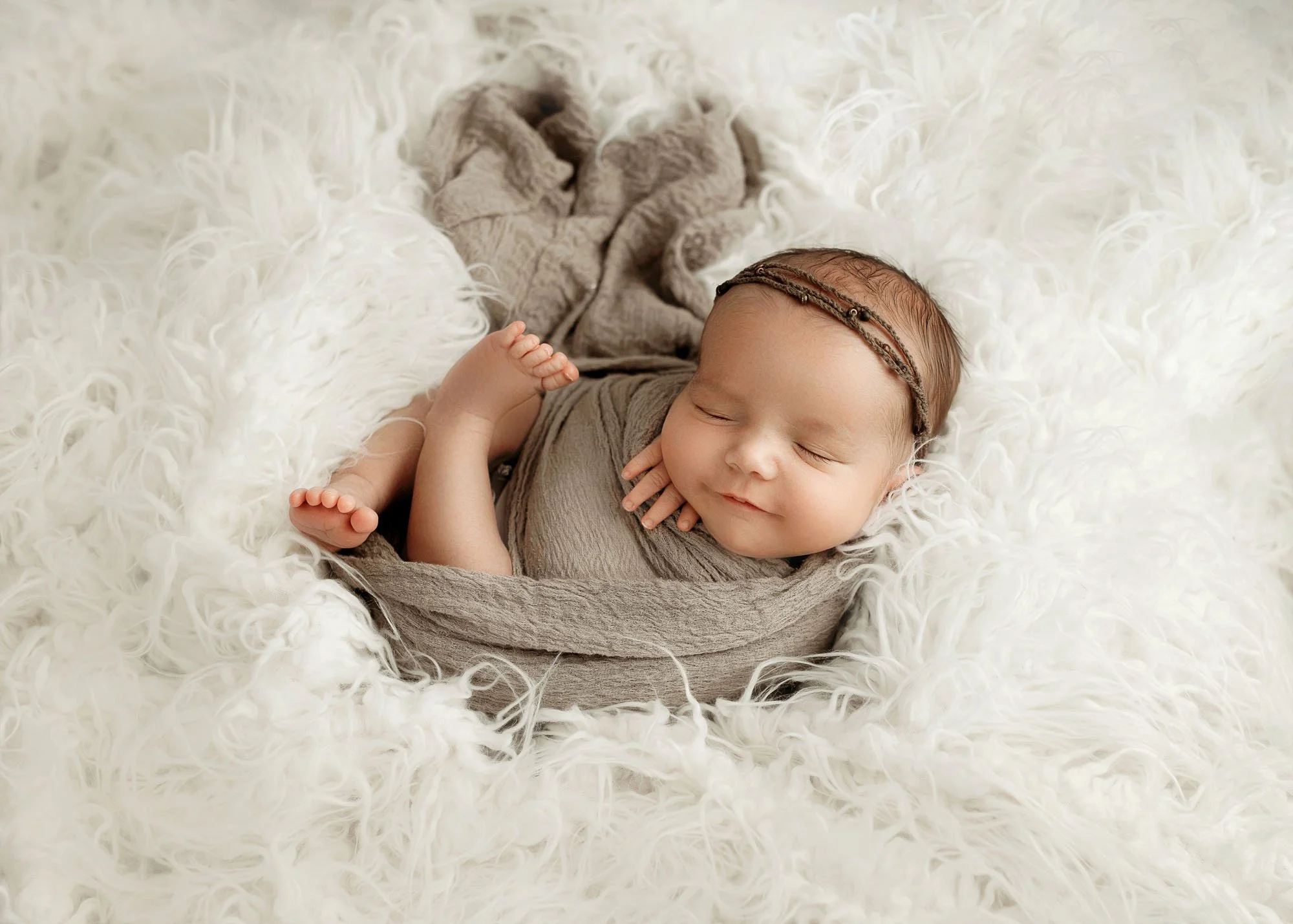 Newborn wrapped in neutral swaddle with legs peeking out