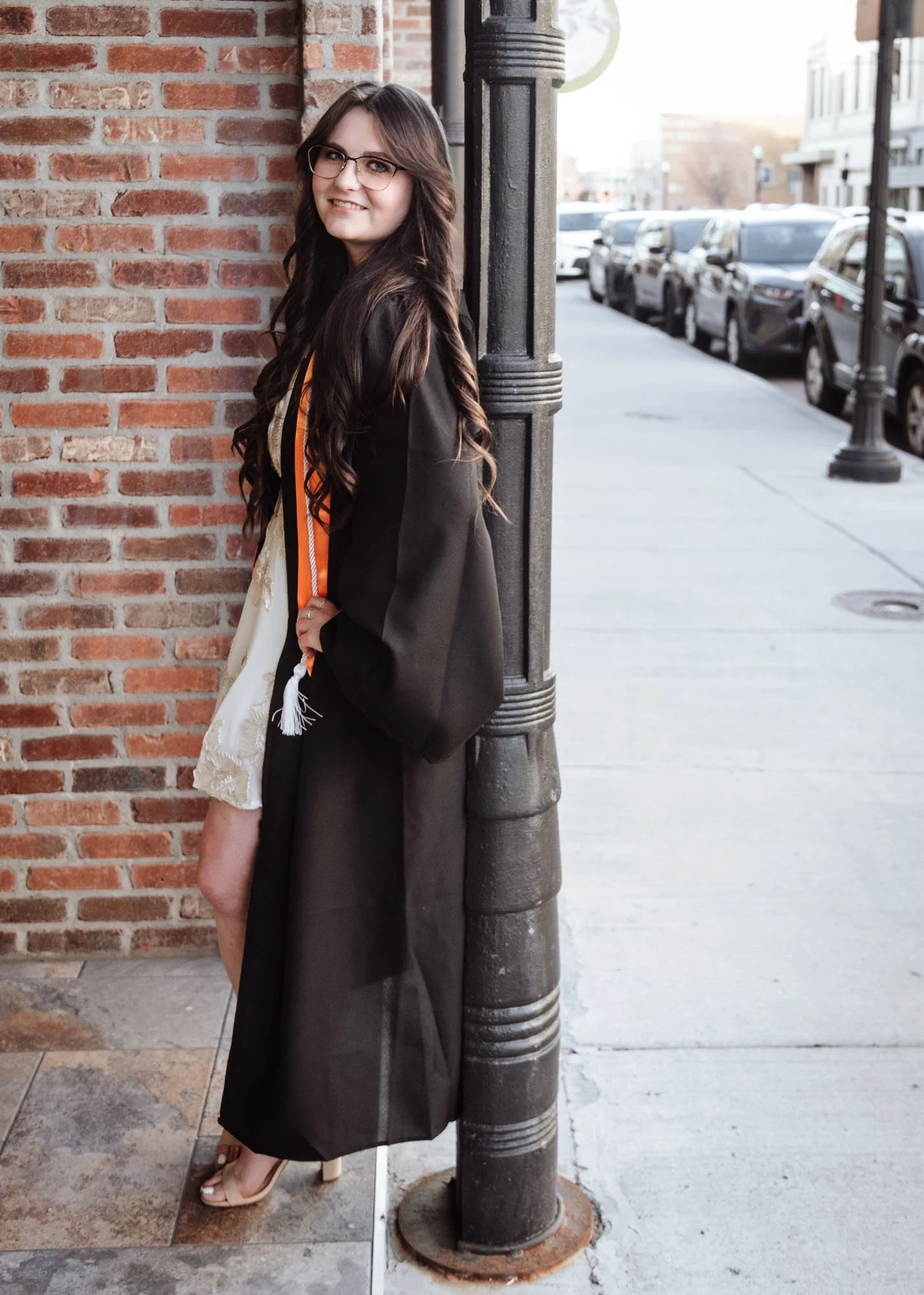 Senior girl in graduation gown posing downtown on brick wall