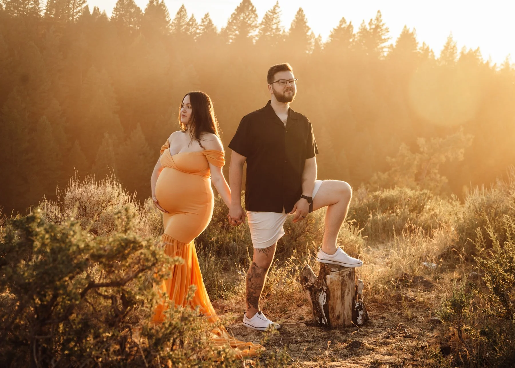 Couple posing at sunset in mountains with pine trees, baby bump visible