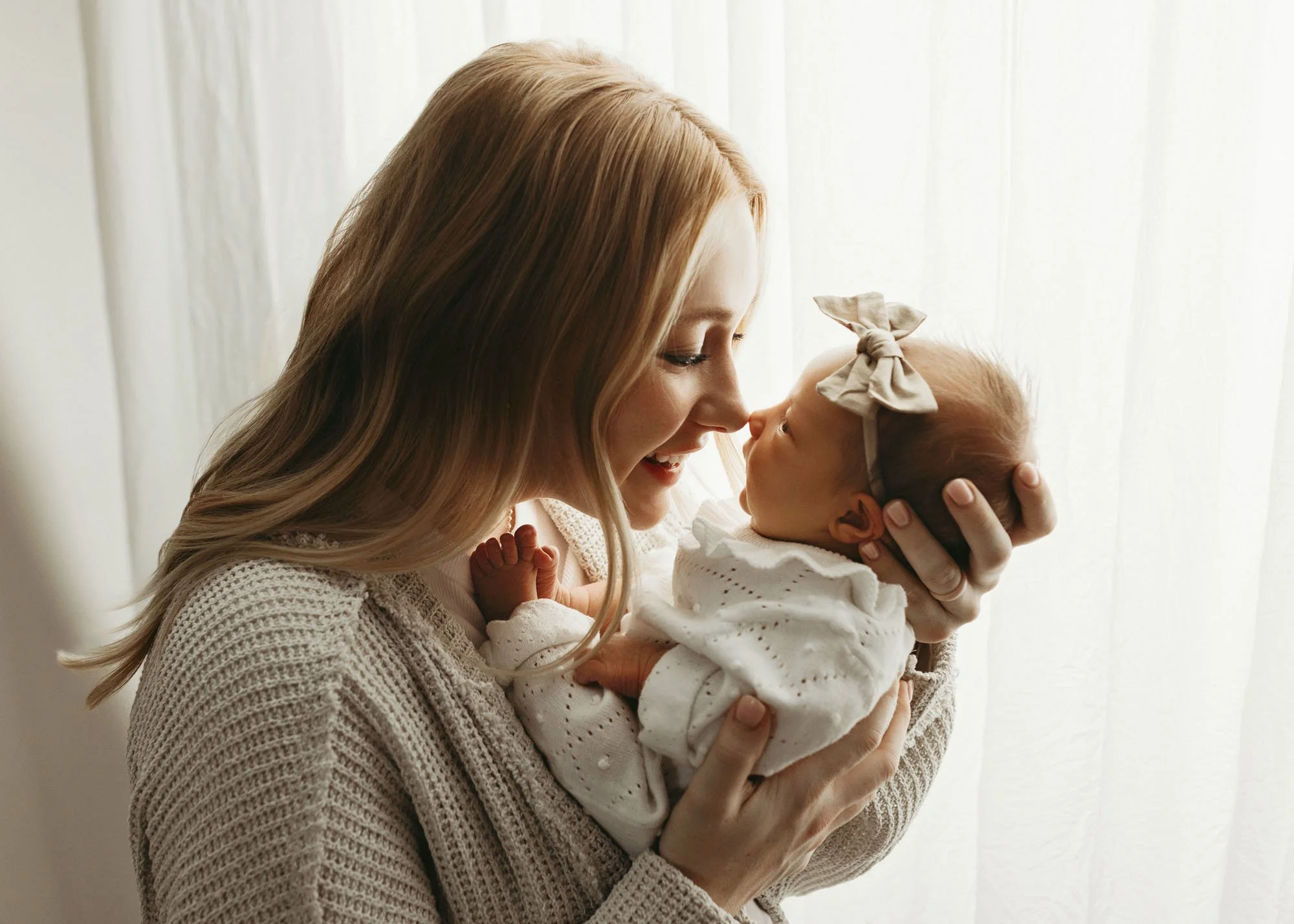 Mother holding newborn on shoulder with soft backlighting in studio