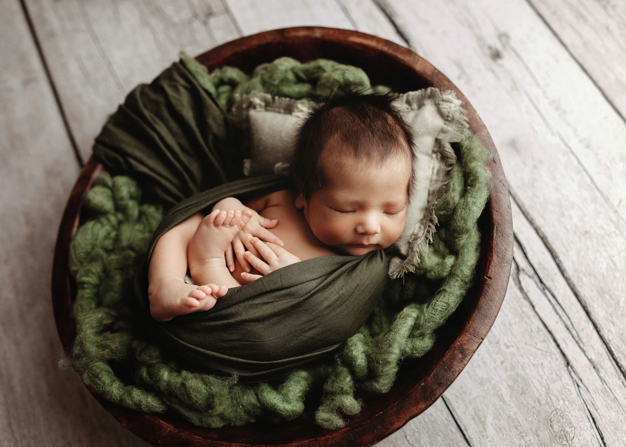 Newborn in tucked in pose wearing knit hat in studio
