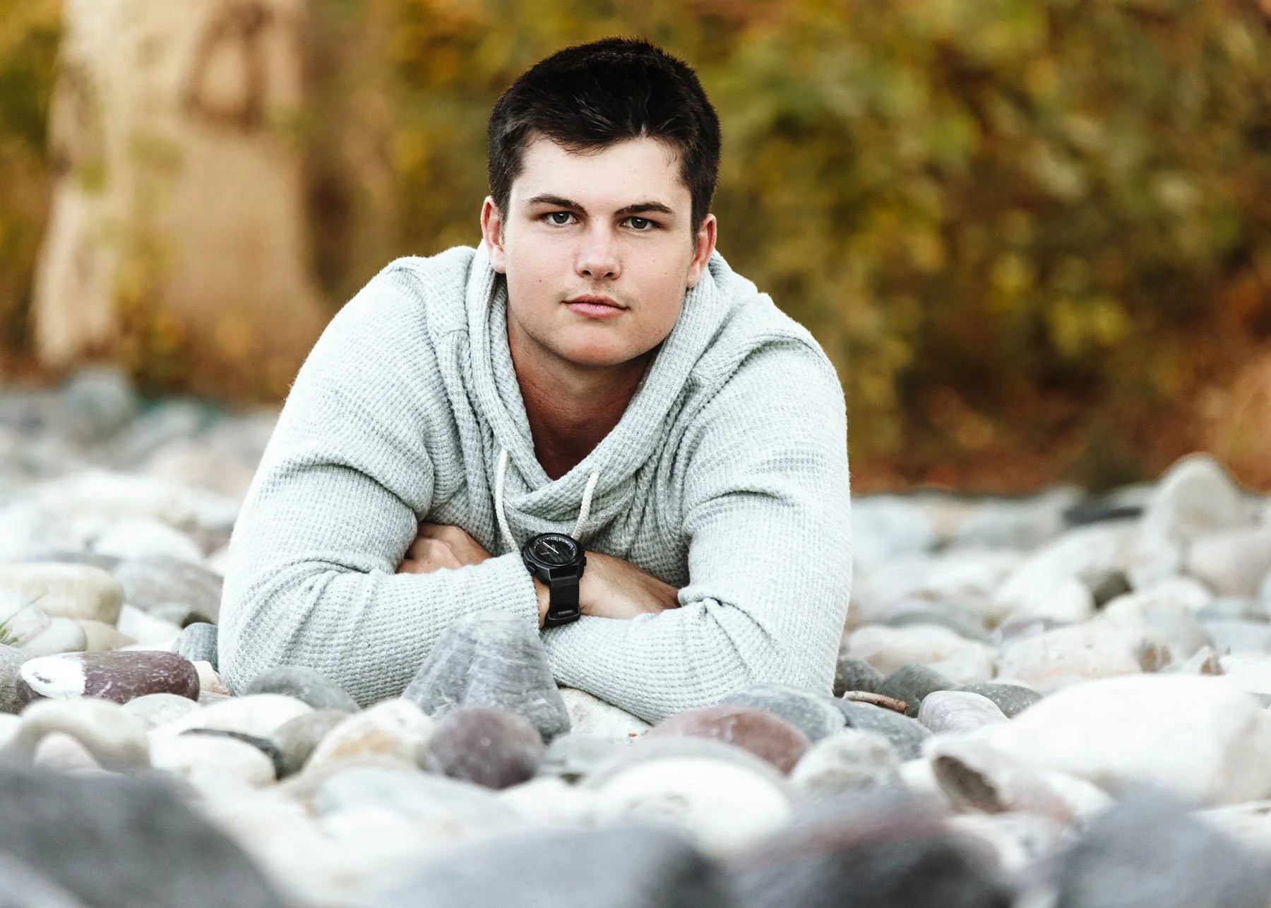 Senior boy lying on stomach in rocky riverbed, arms folded