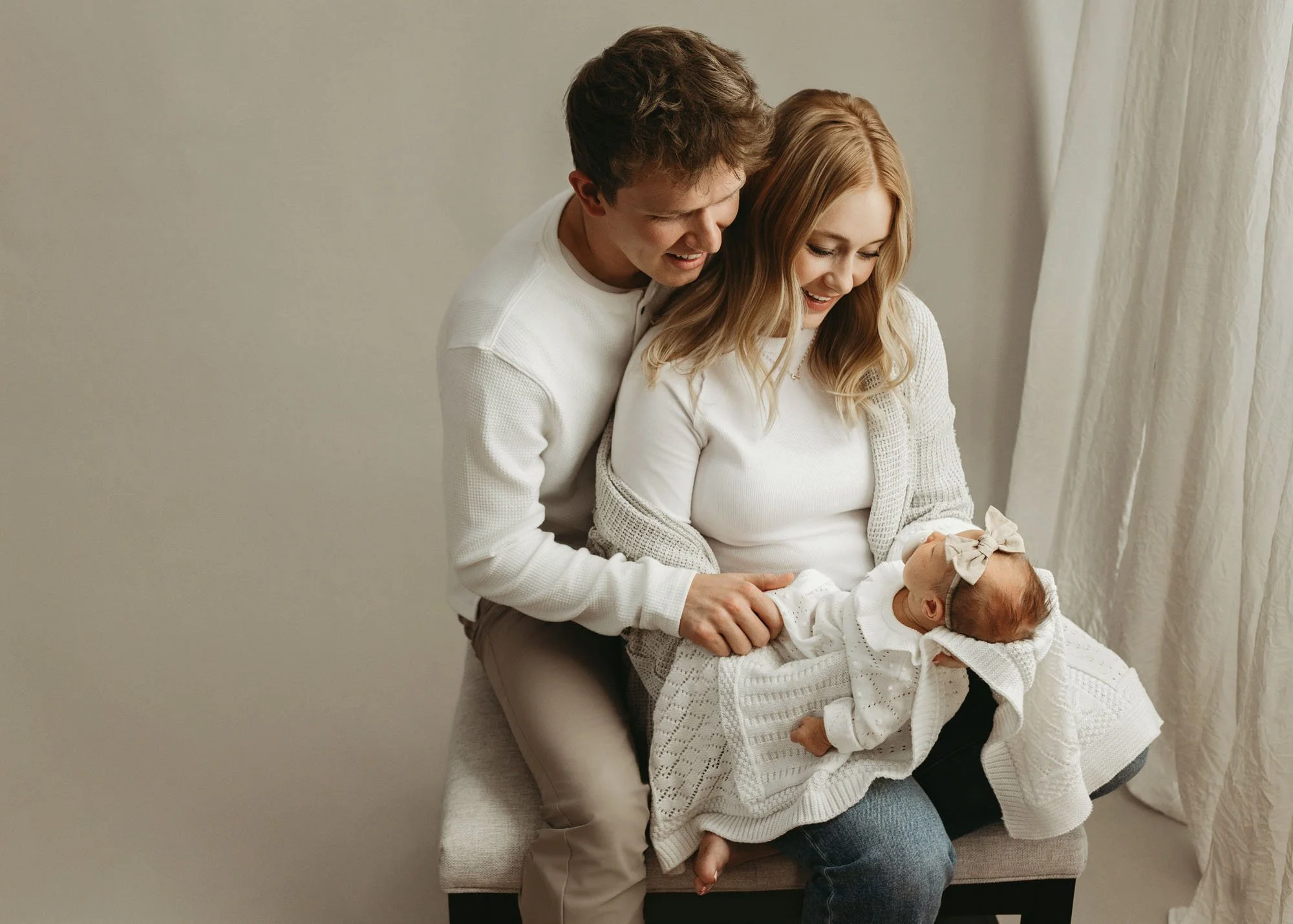 Mother holding newborn with father standing behind both looking at baby