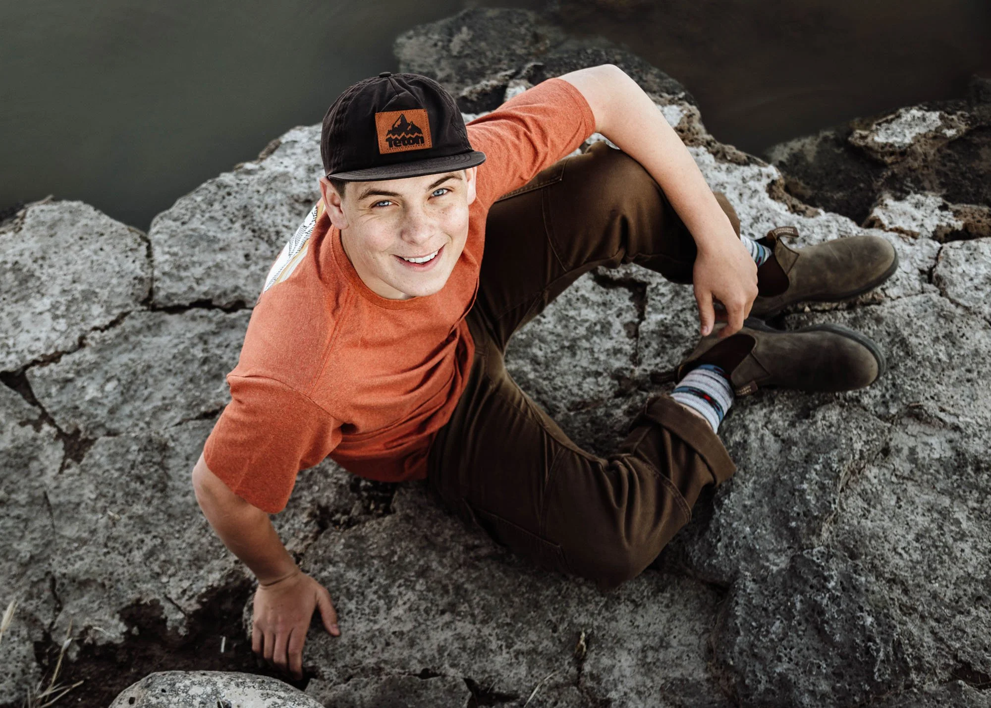 Senior boy sitting on rocks looking up during outdoor portrait