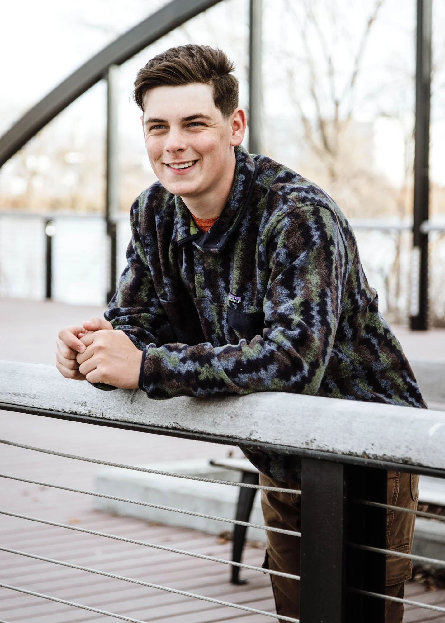 Teen boy leaning over rail of fence for senior portrait