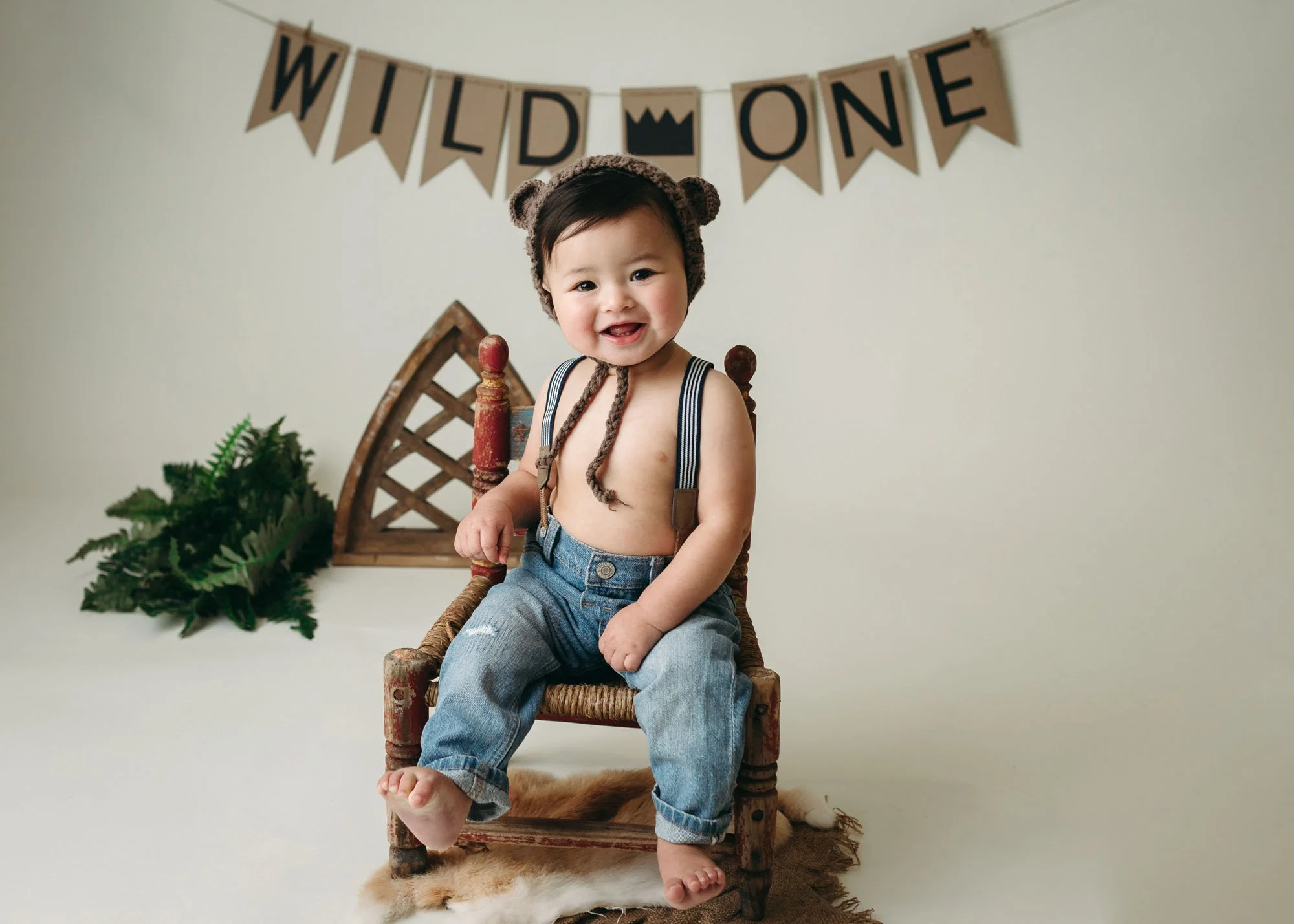 Baby sitting on rustic wooden chair in white studio