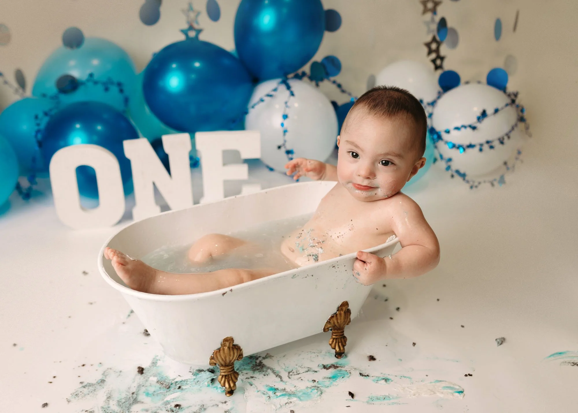 One year old cake smash with bold blue balloons and frosting