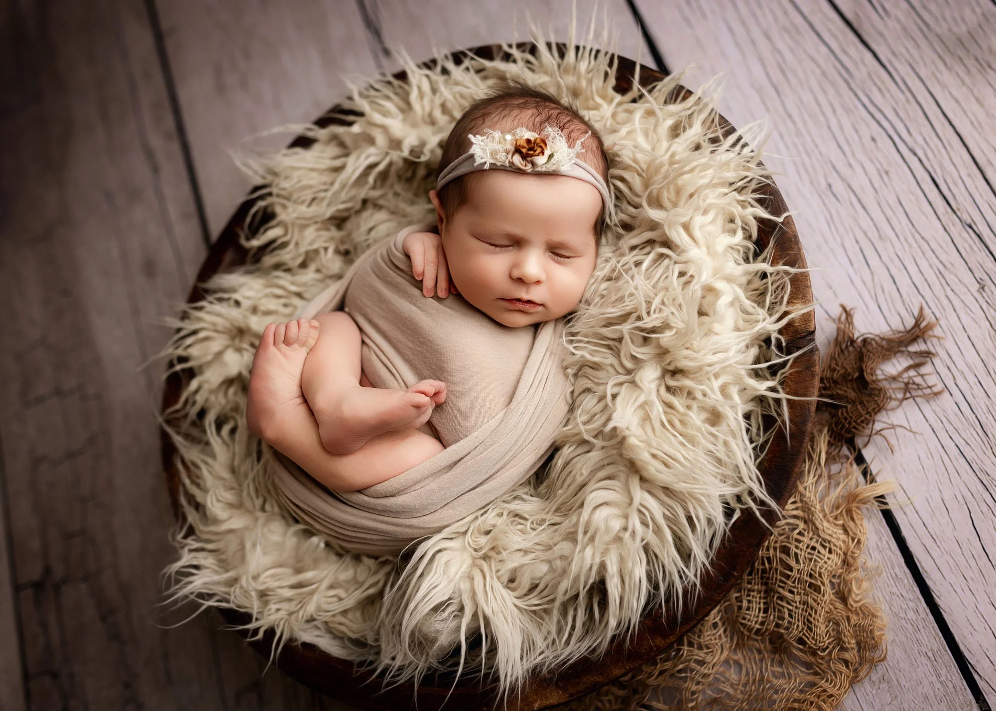 Newborn wrapped in neutral swaddle laying on back with arms up in studio