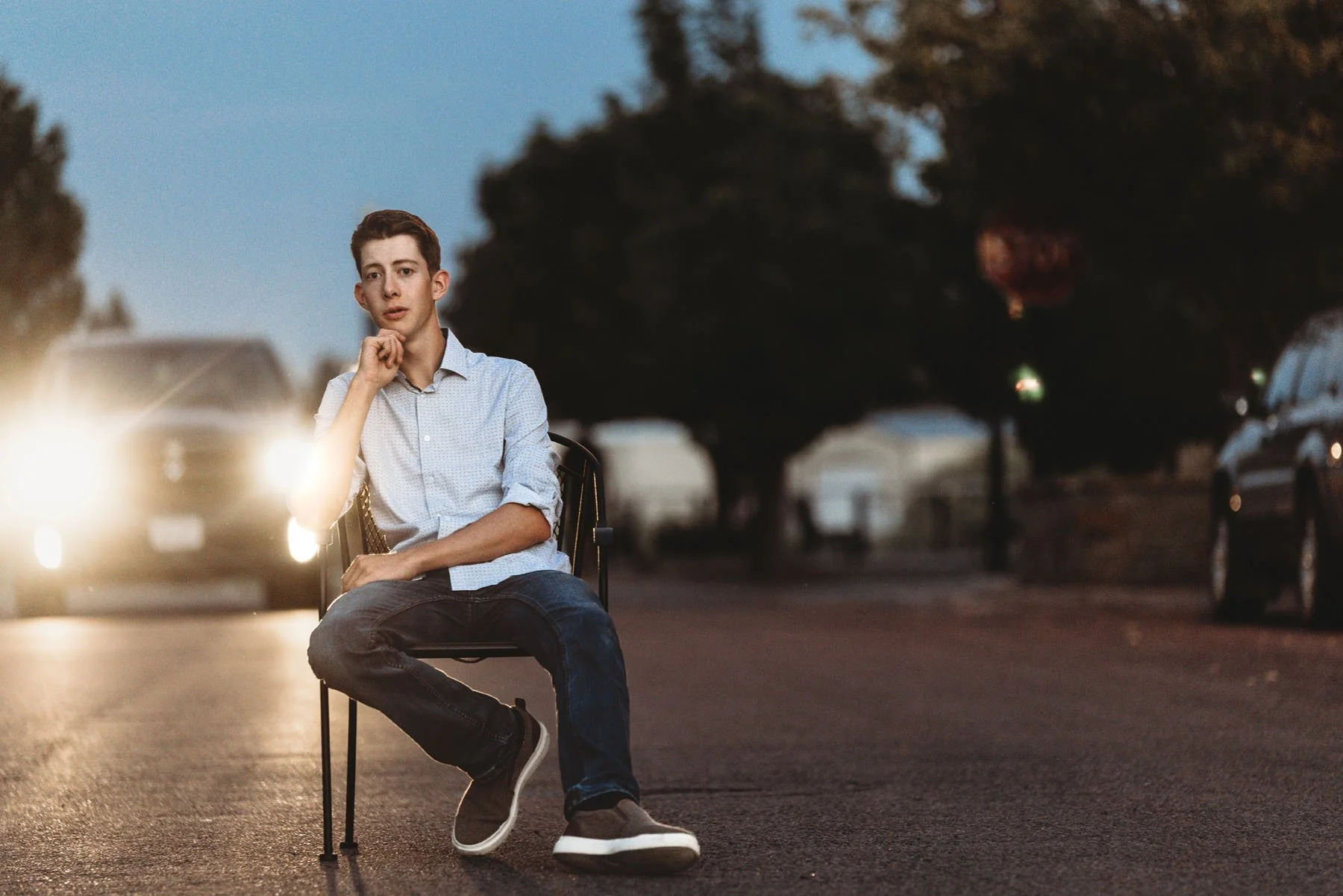 Teen boy sitting on chair in middle of road with car headlights behind