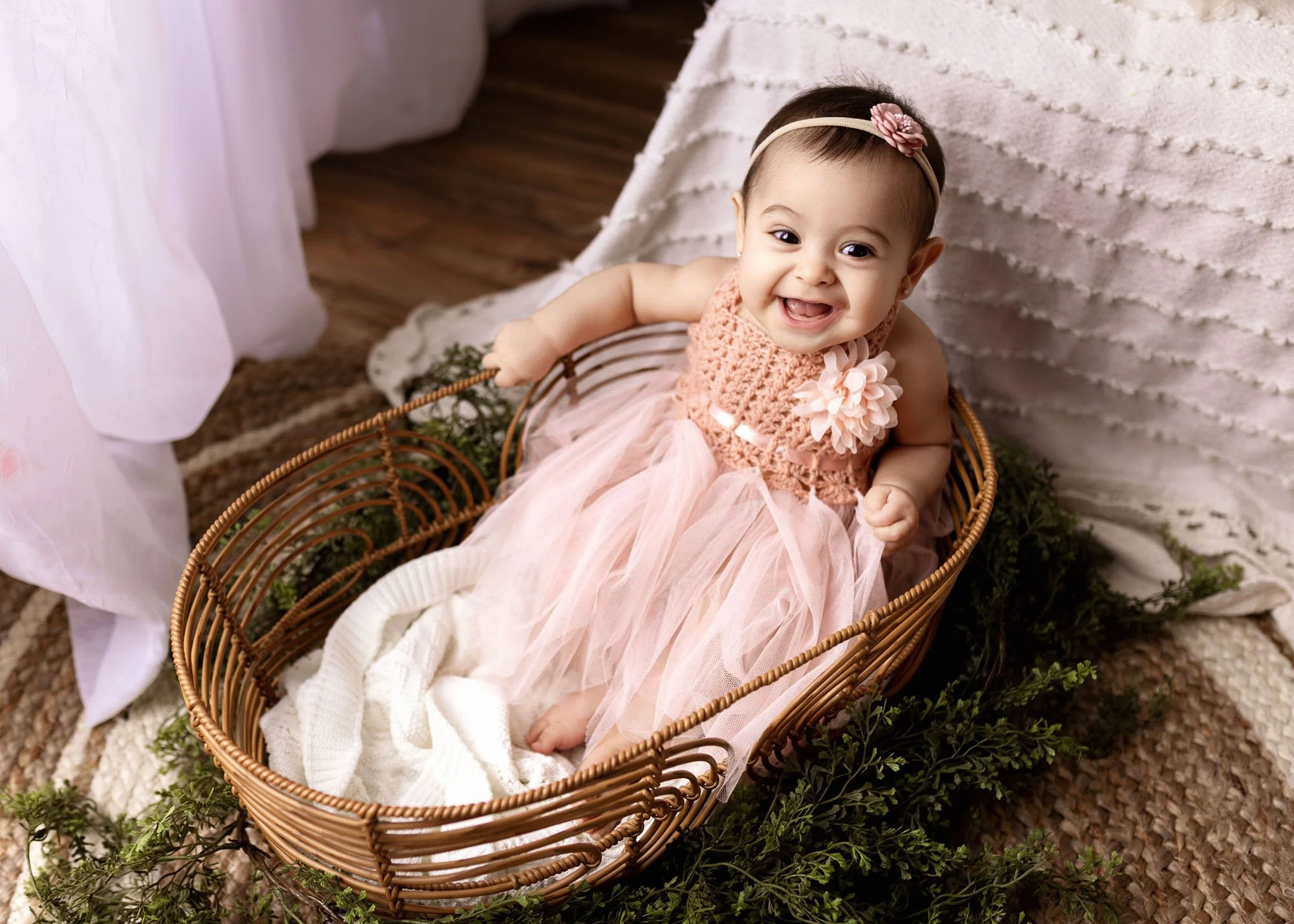 Baby sitting and smiling in Moses basket in studio