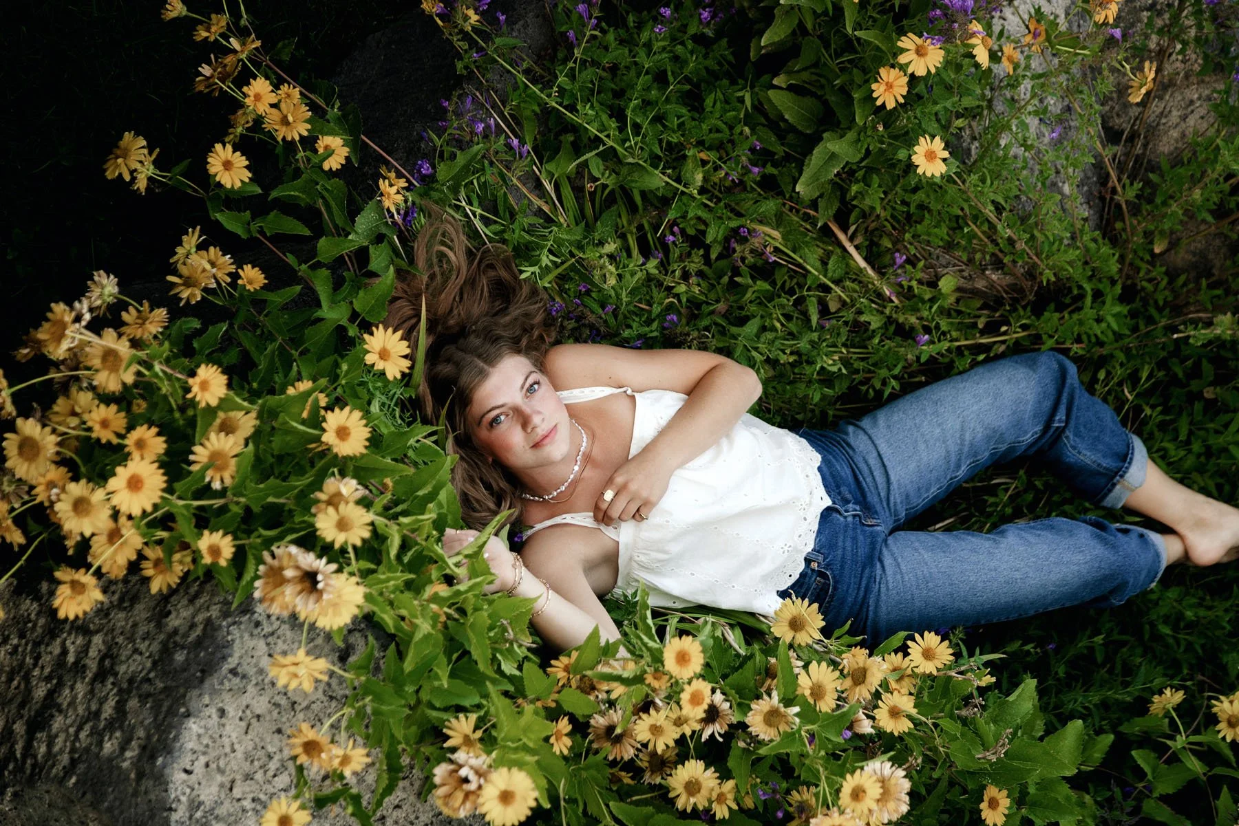 Senior girl laying in field of yellow flowers smiling