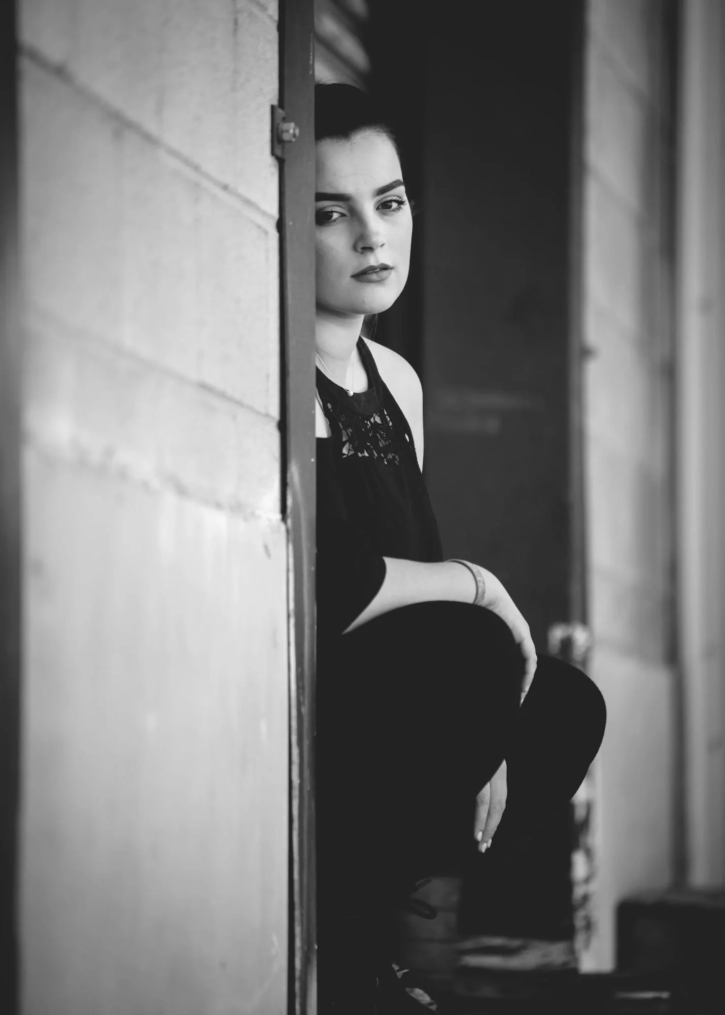Senior girl in black and white hiding against wall for artistic portrait