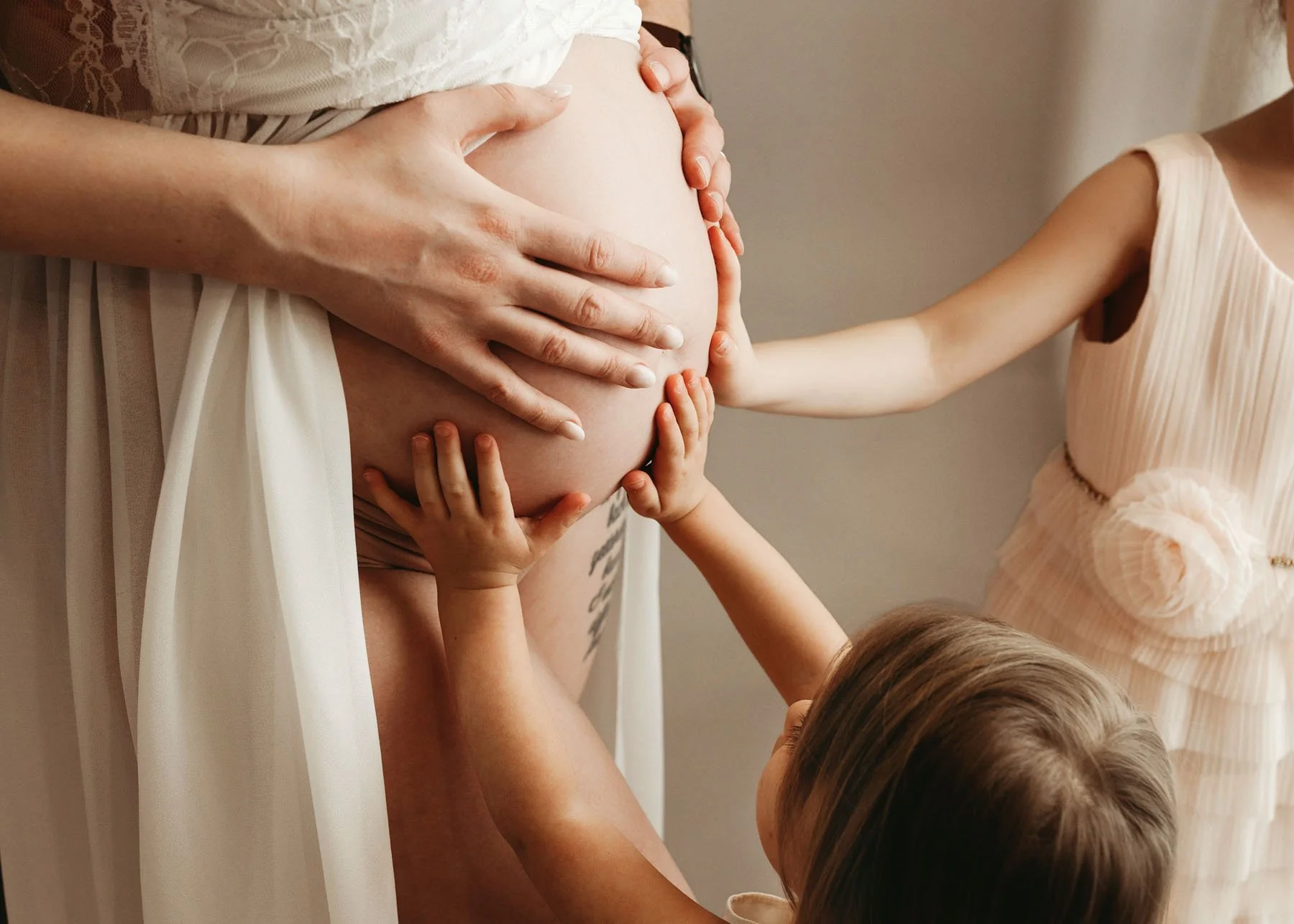 Exposed baby bump with all family hands resting on mama's tummy