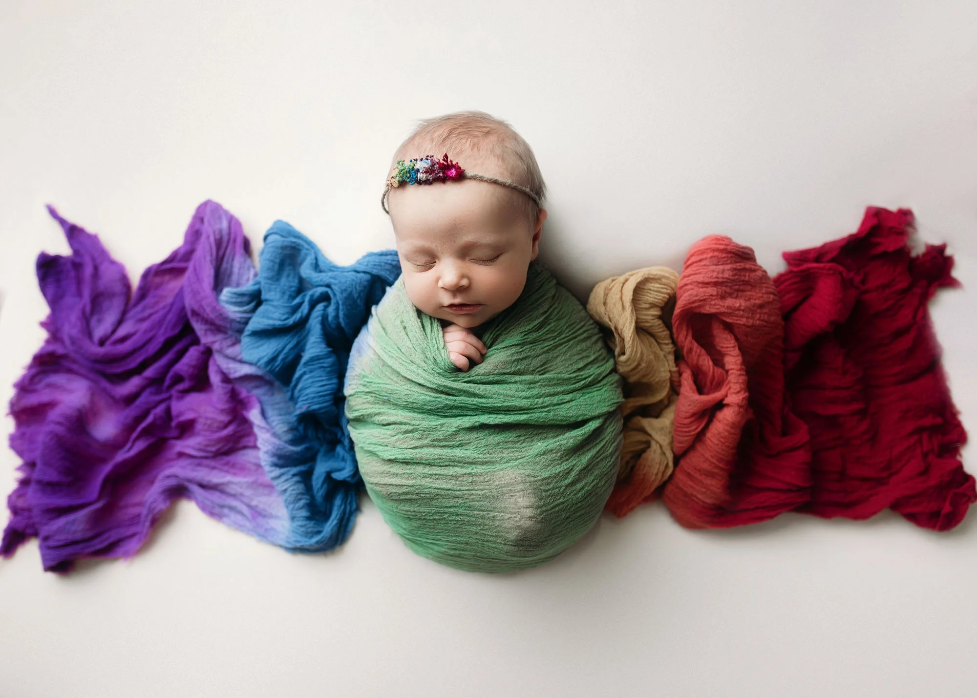 Newborn wrapped in rainbow swaddle posed in bucket prop