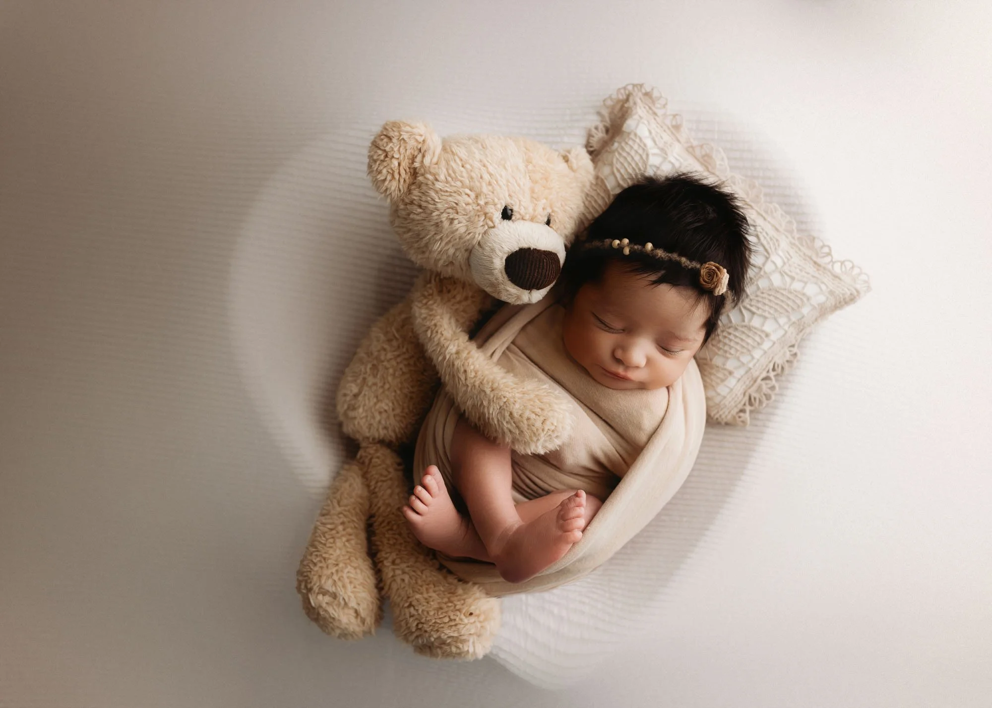 Newborn in heart bowl with teddy bear prop hugging baby
