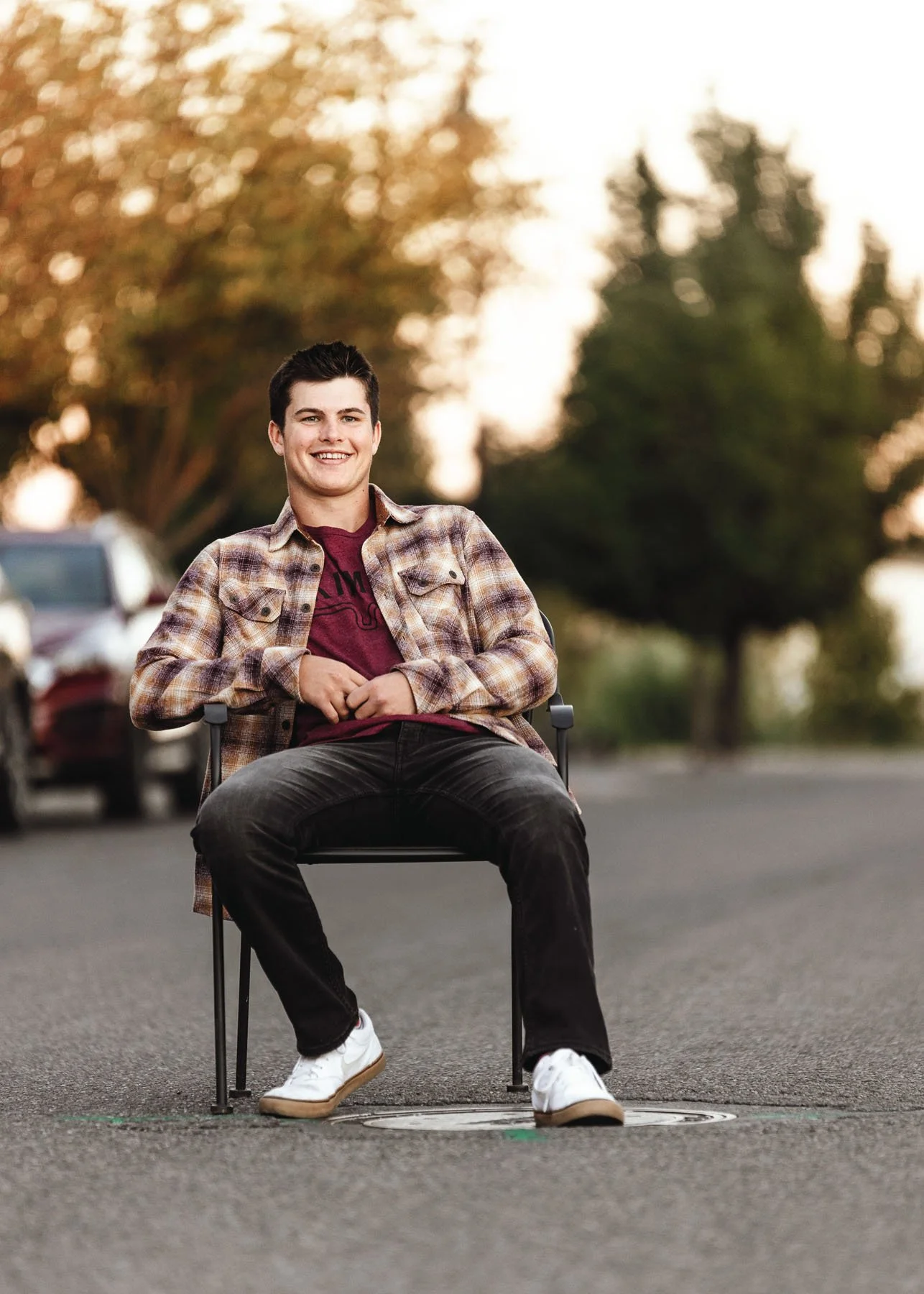 Senior boy sitting on chair wearing plaid shirt outdoors