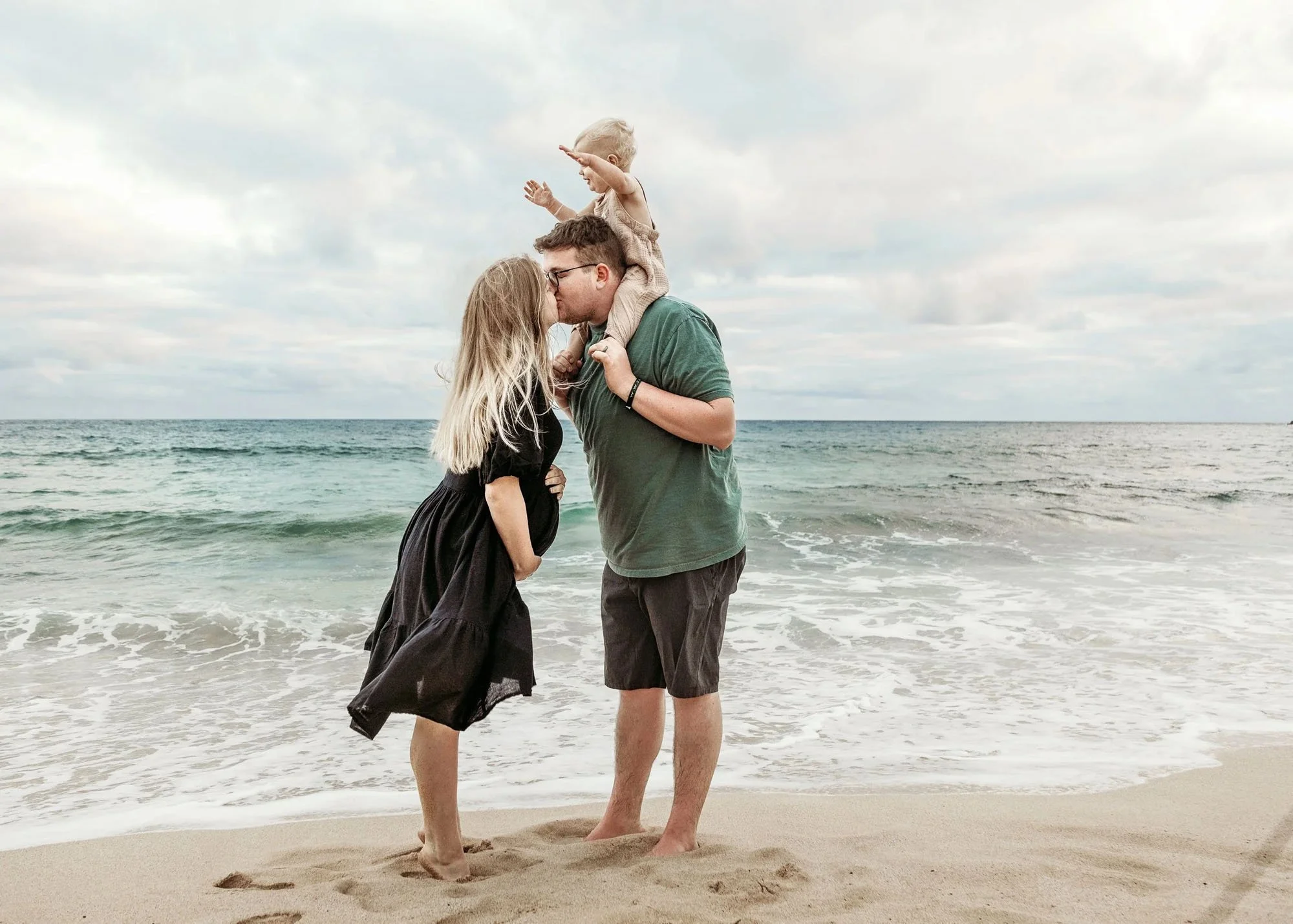 Close-up of pregnant belly with toddler feet in sand and ocean in background