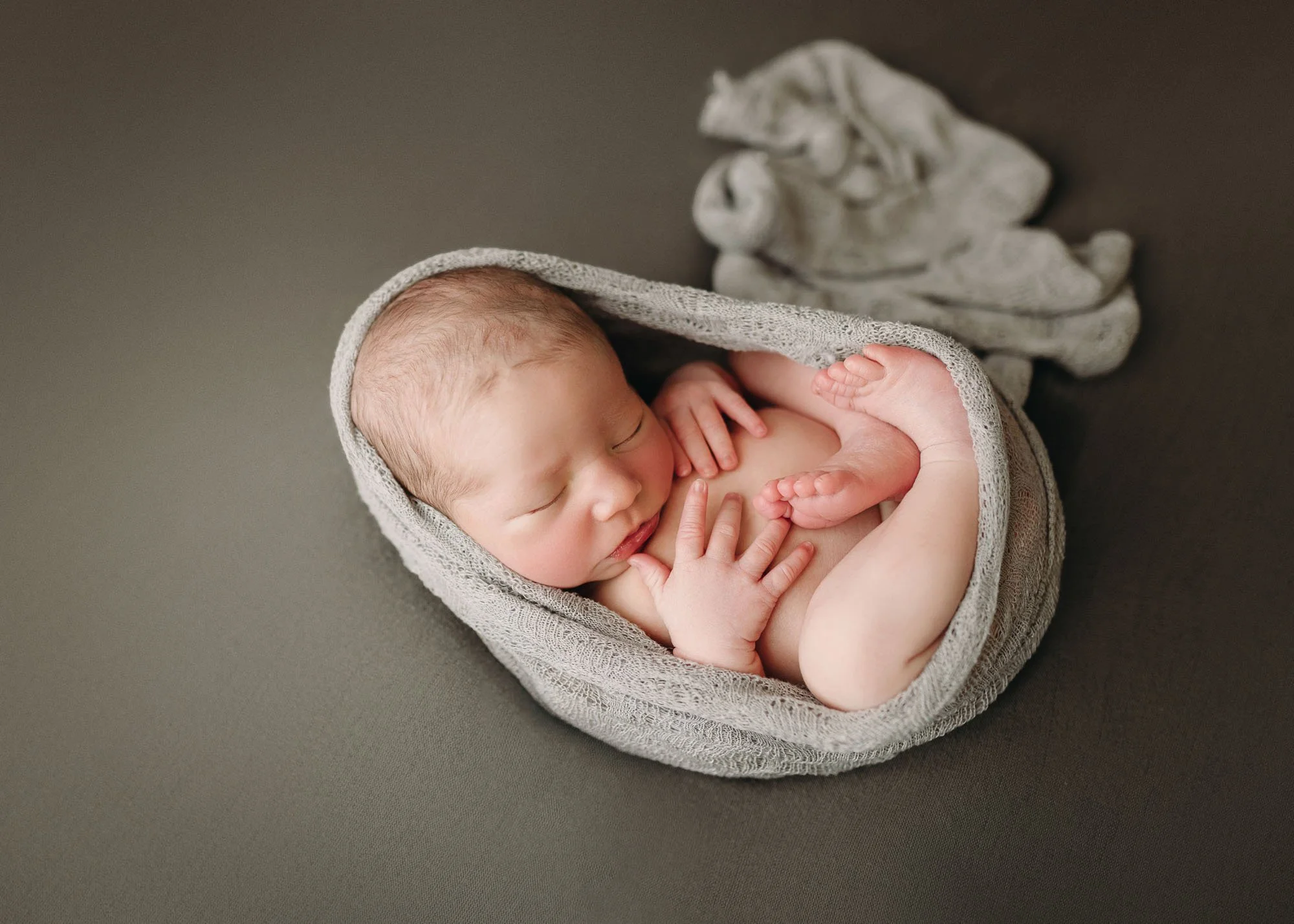 Newborn in egg pose wrapped snugly with arms and legs visible