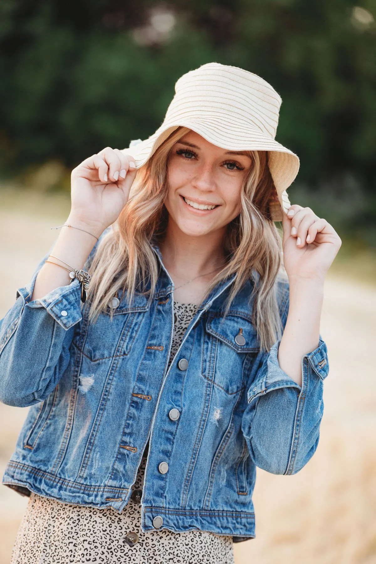 Senior girl holding hat smiling in wheat field