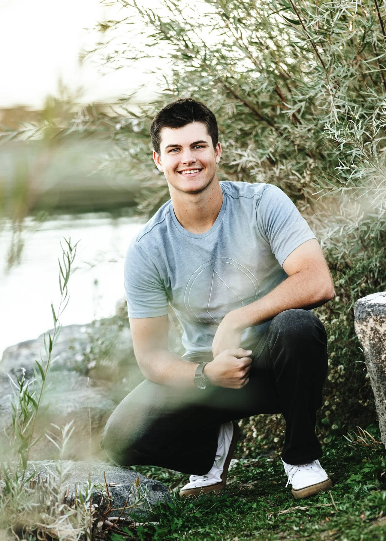 Senior boy in blue shirt posing by river during outdoor session