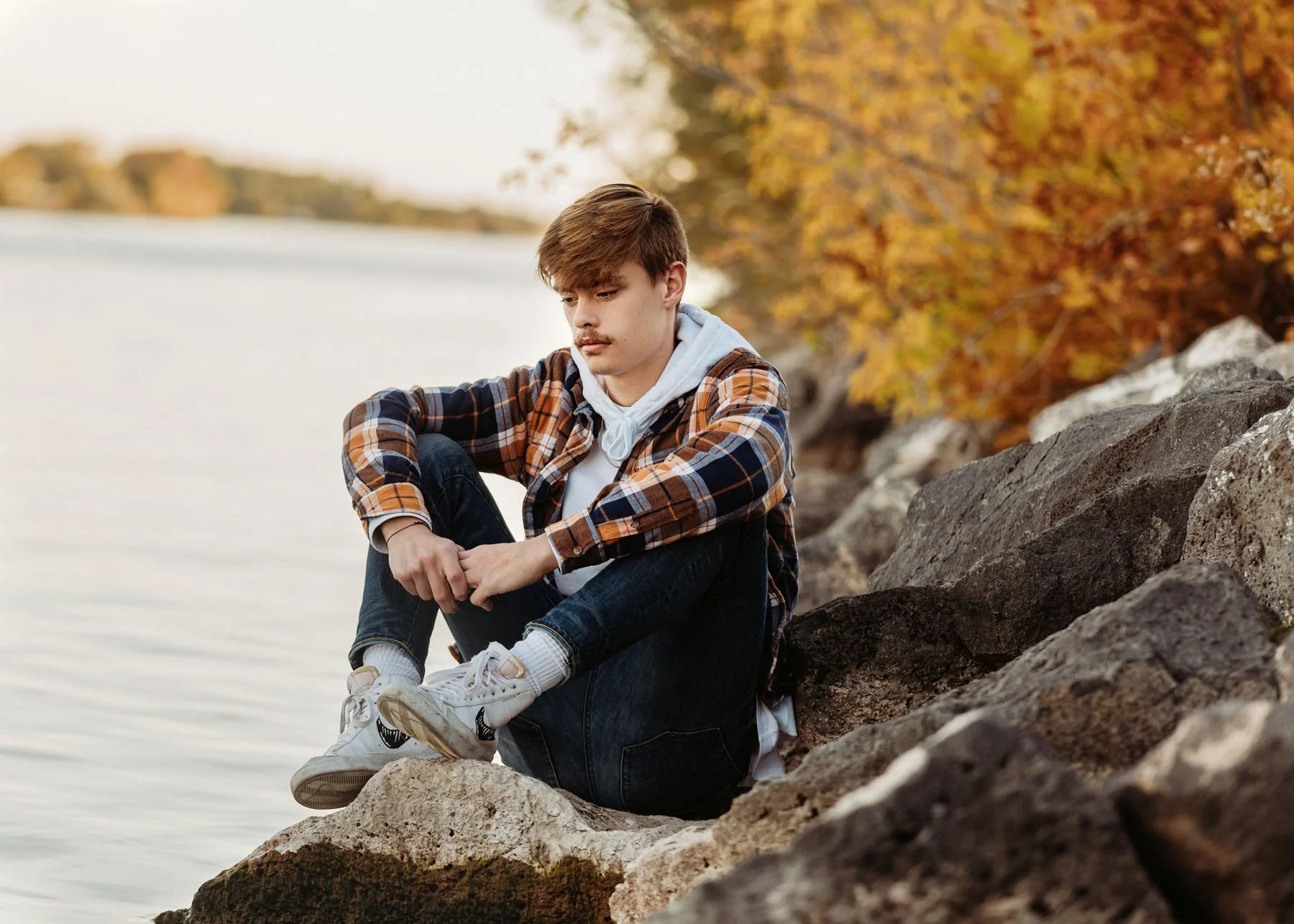Boy in plaid shirt posing by river for senior portrait