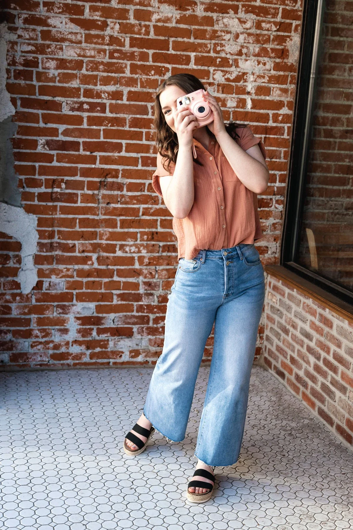 Senior girl taking picture with camera in brick outdoor session