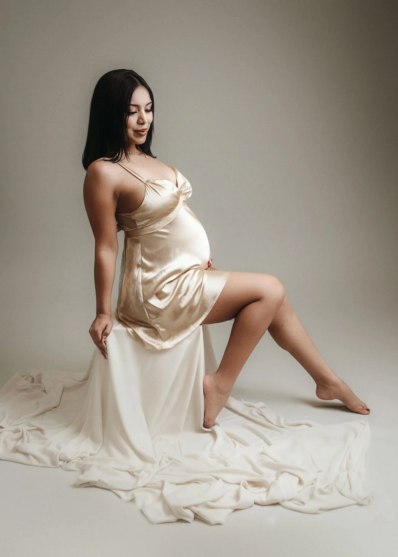Pregnant mama in white wrap sitting on floor with legs crossed, hand on tummy, shot from above